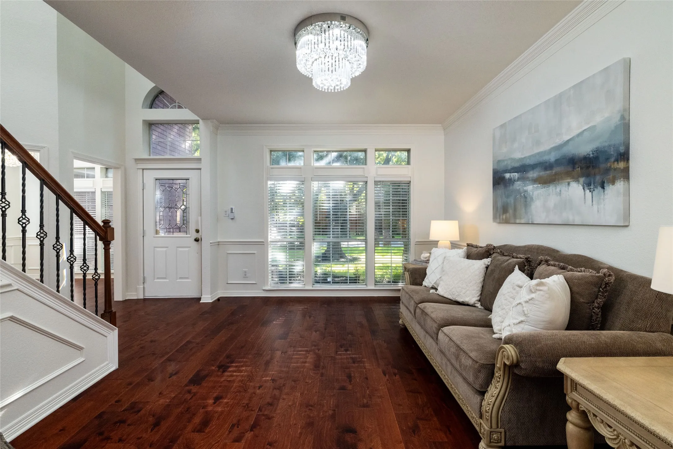 Hardwood flooring throughout, a detailed staircase with wrought iron balusters, natural light from multiple windows, crown molding, and a decorative ceiling light fixture