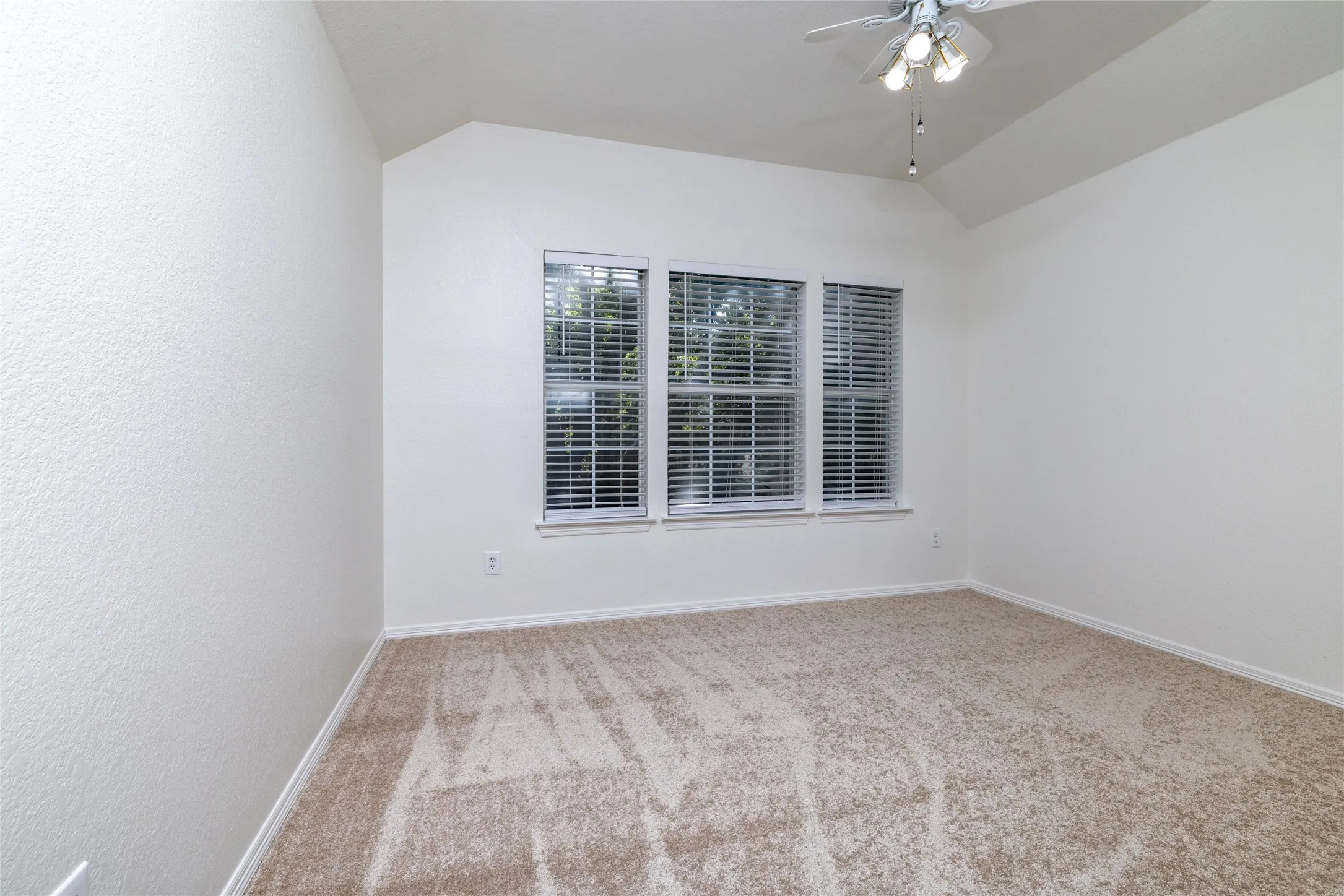 Carpeted room with a vaulted ceiling, three windows with blinds, and a ceiling fan with integrated lighting