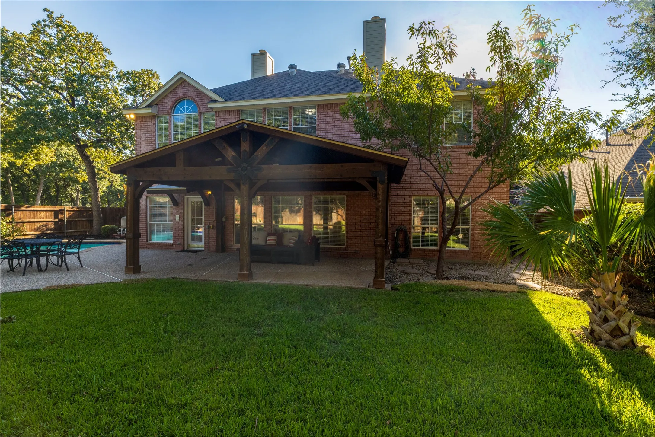 Brick exterior with multiple windows, covered patio featuring exposed wood beams, and a concrete patio surrounding a pool
