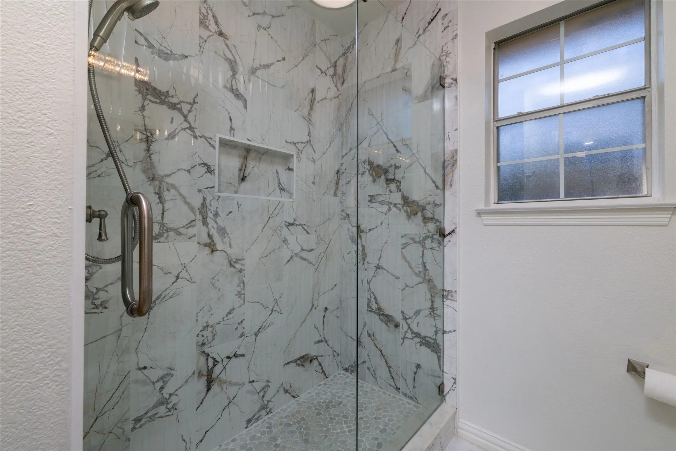 Glass-enclosed shower with marble-finish tile, integrated shower niche, and mosaic tile floor