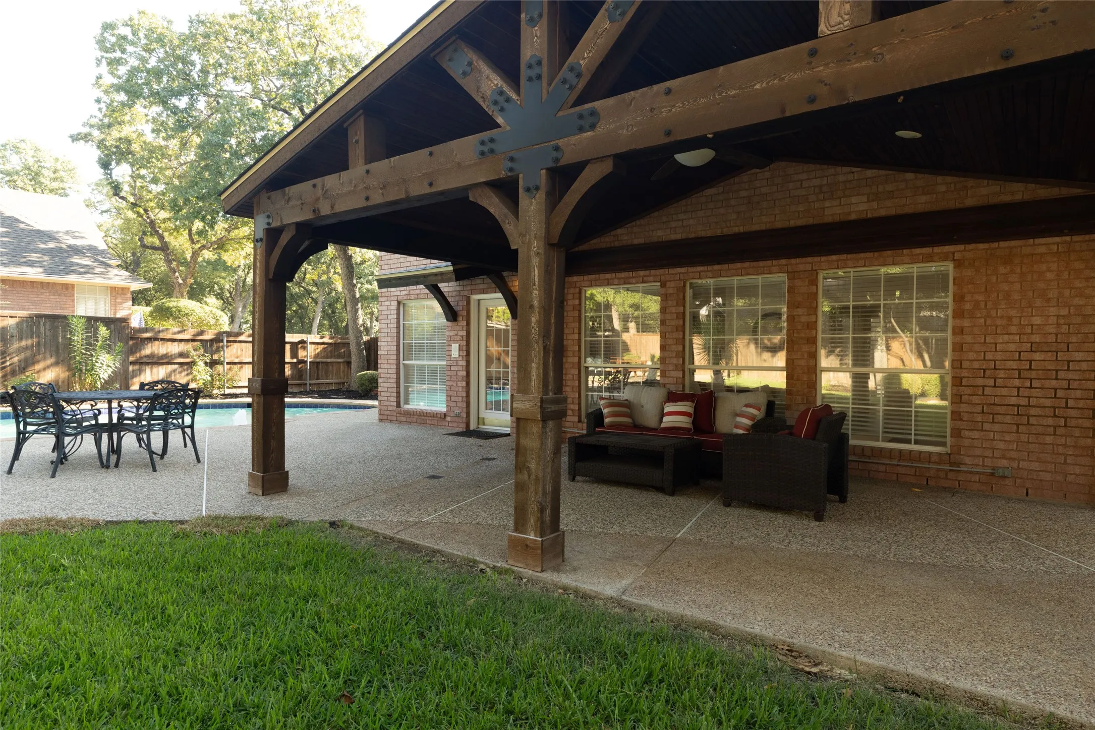 Expansive outdoor living area featuring a covered patio, exposed aggregate concrete, and a swimming pool