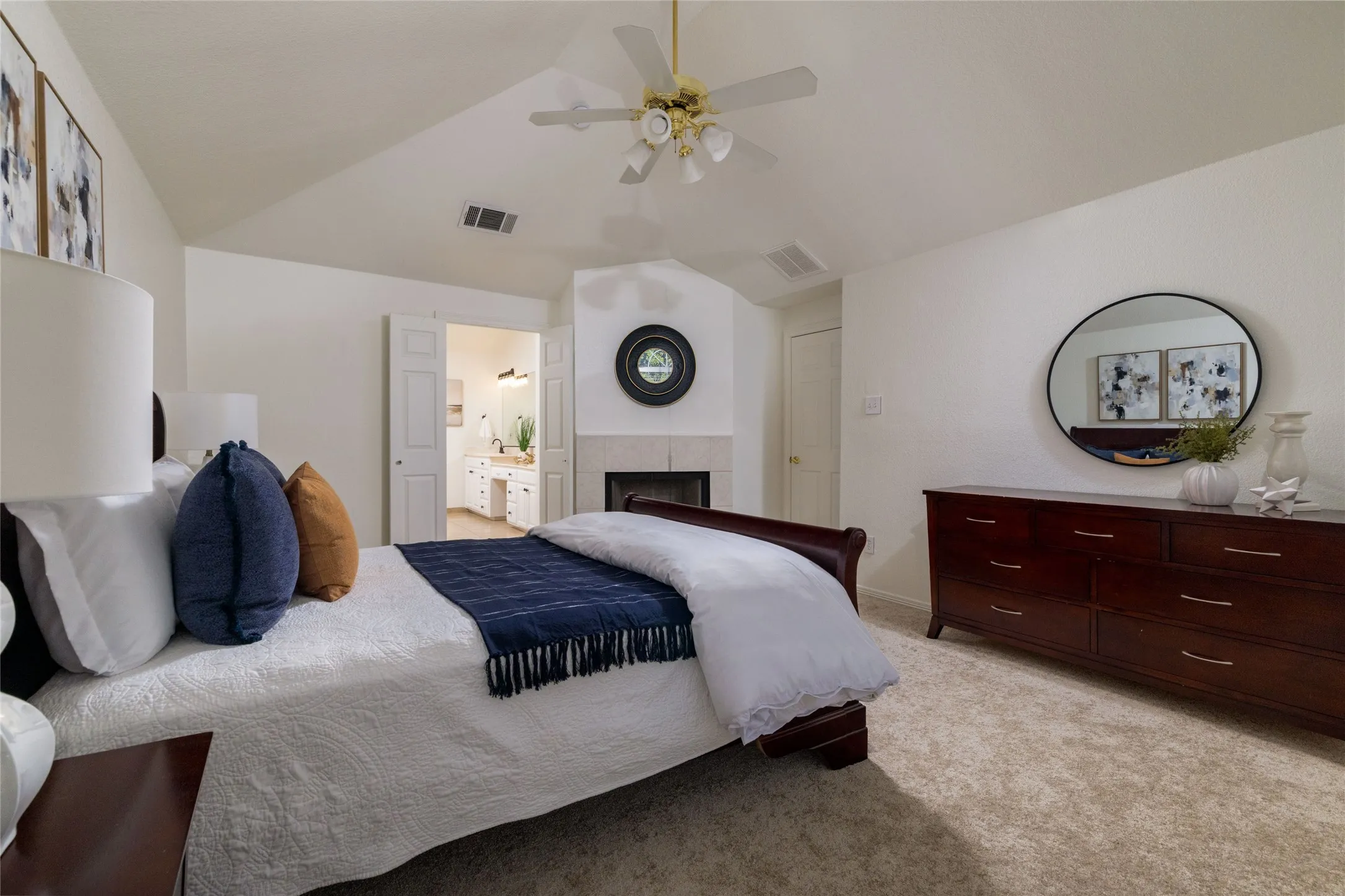 Vaulted ceiling with a ceiling fan, carpet flooring, a built-in fireplace with a stone surround, and an adjacent bathroom with a double vanity
