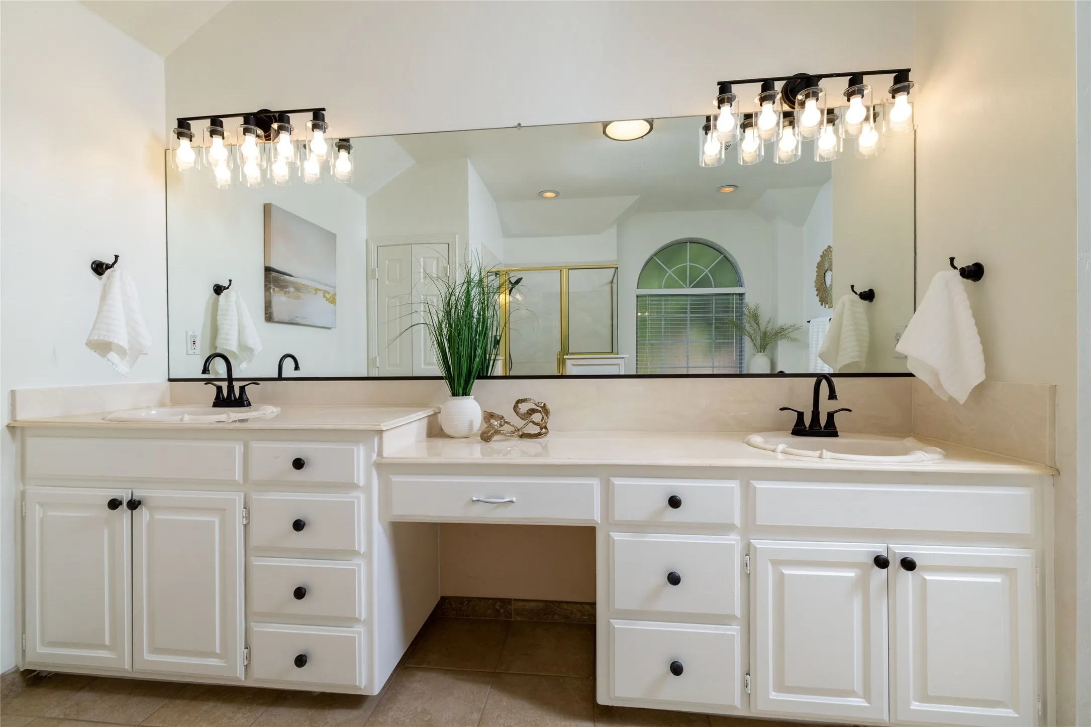 Dual vanities with integrated sinks, ample storage cabinetry, and a dedicated vanity area under a large wall-mounted mirror