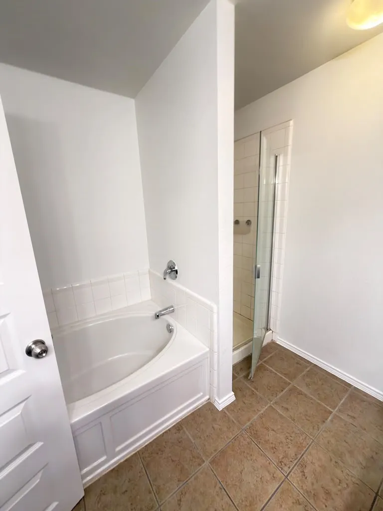 White soaking tub with chrome fixtures, glass-enclosed shower, and tile flooring