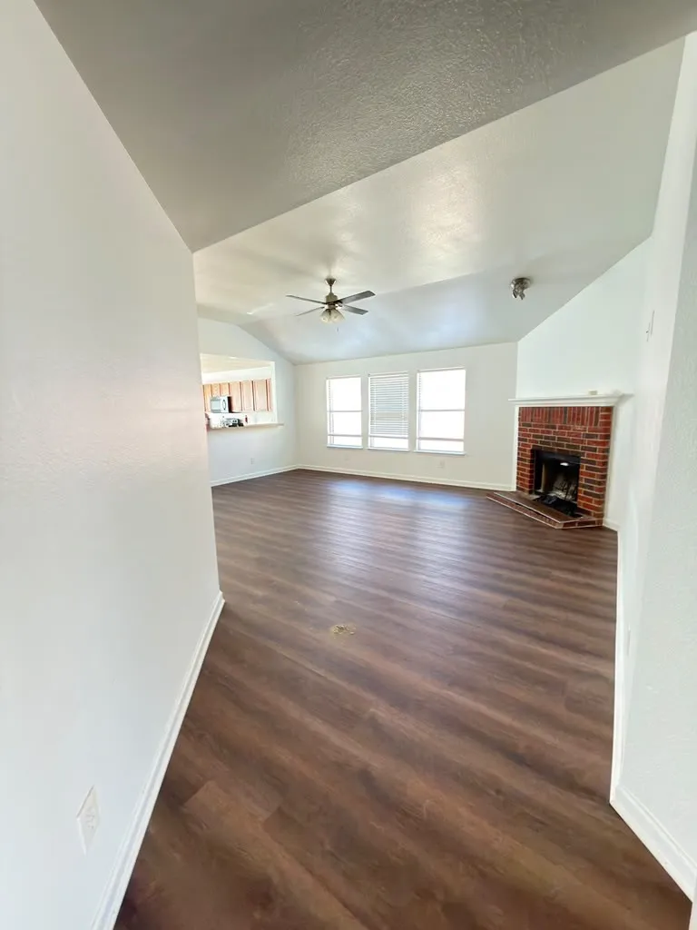 Vaulted ceiling with a ceiling fan, wood-finish flooring, multiple windows, and a brick fireplace with a white mantel