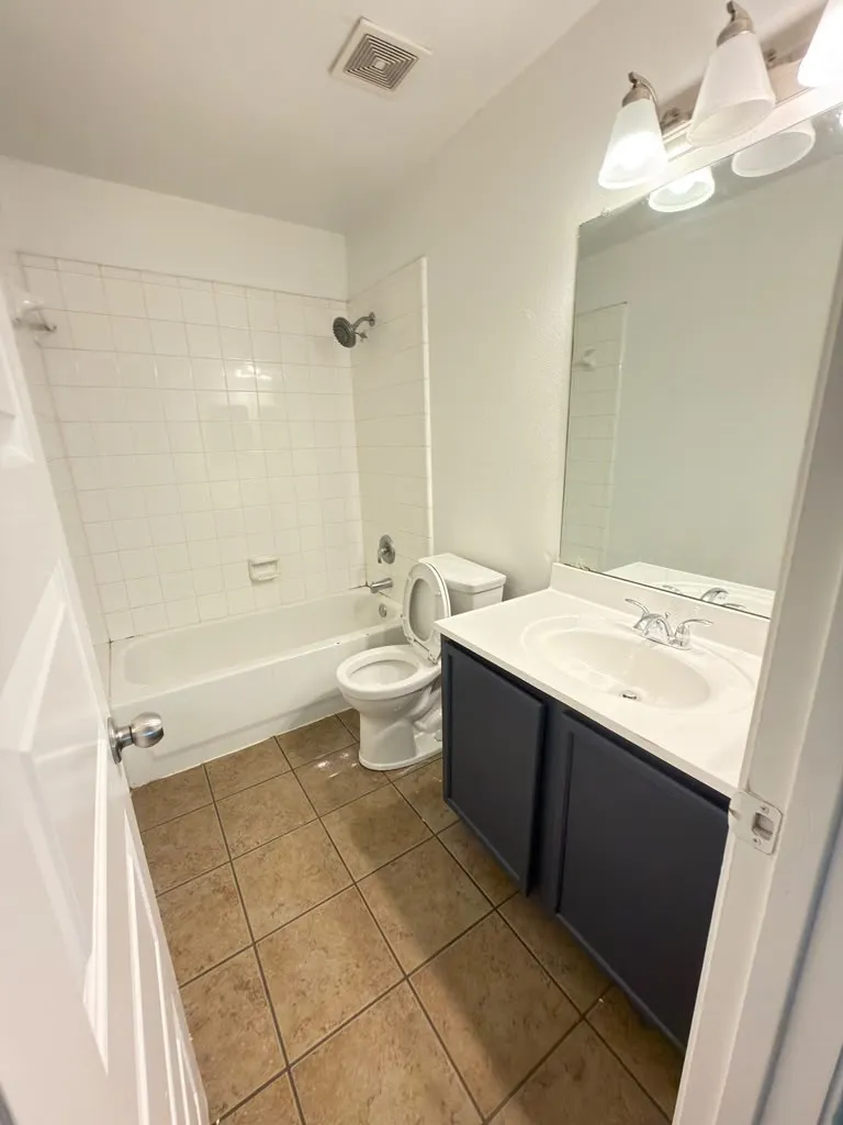 Bathroom featuring a white tub, white tiled shower surround, a vanity with a white countertop and dark cabinetry, and tile flooring