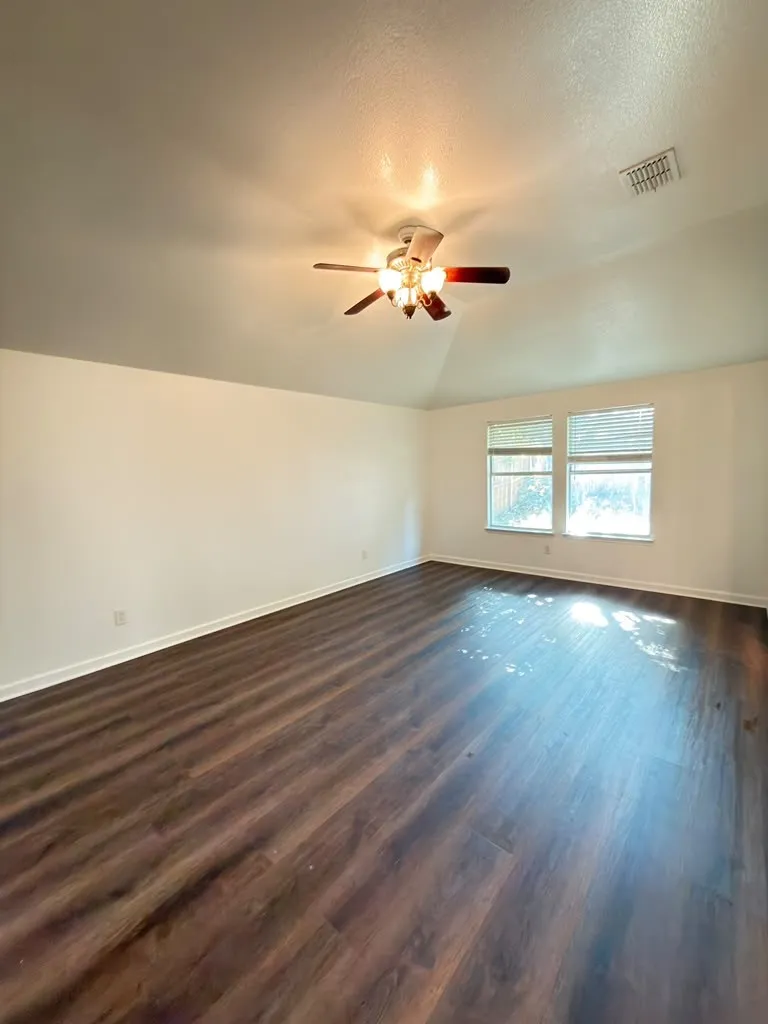 Vaulted ceiling with a flush-mount ceiling fan, rich wood-finish flooring, and dual windows