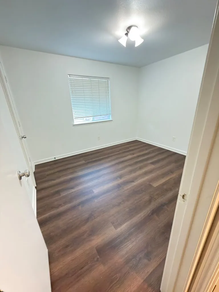 Spacious room featuring wood-finish flooring, white walls, and a window with blinds