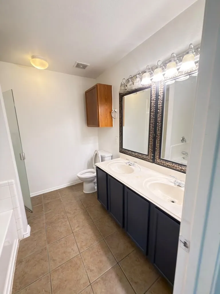 Tiled flooring, dual vanity with undermount sinks, wood-finish wall cabinet, framed mirrors, and a shower/tub combination