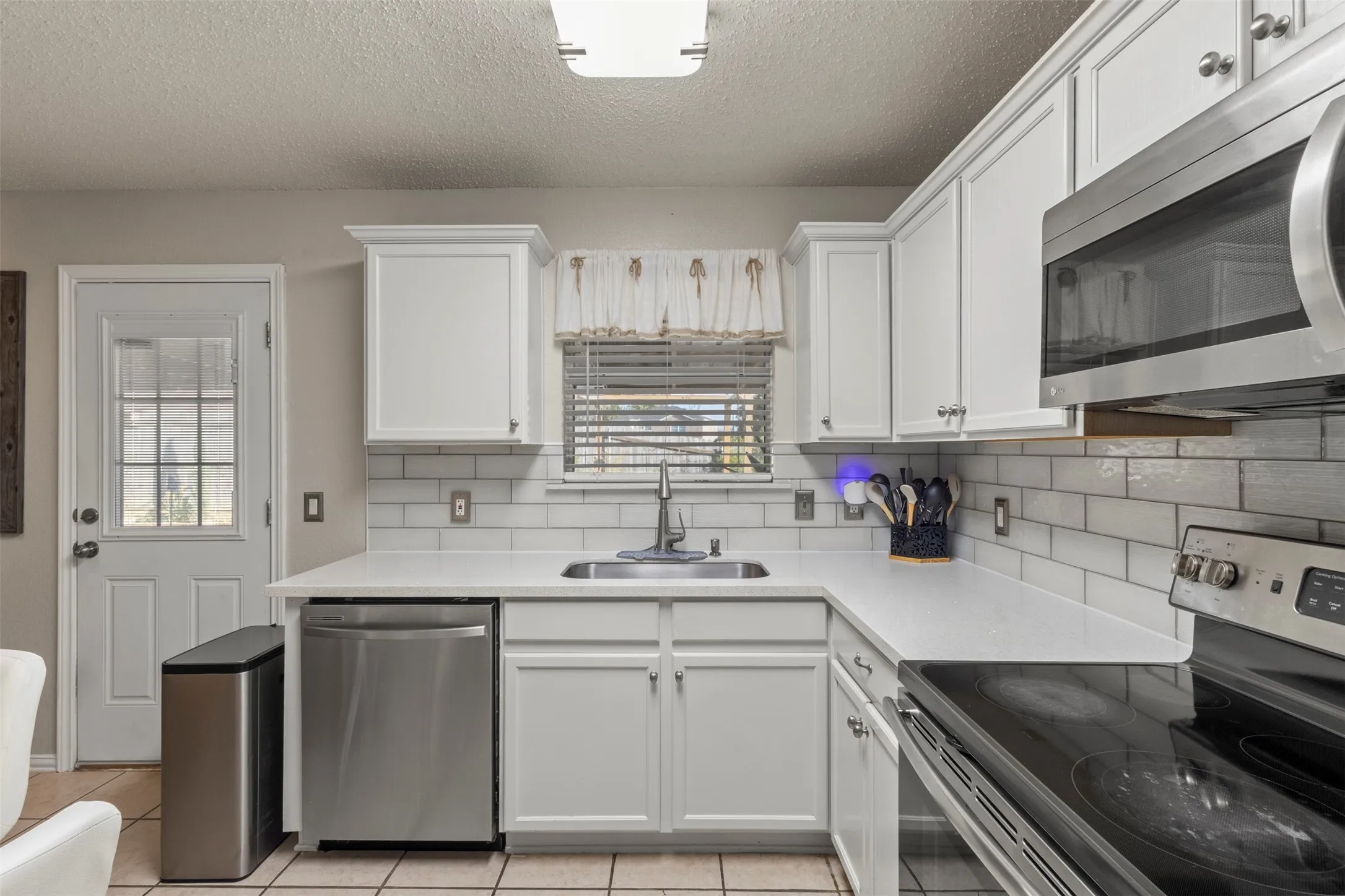 White cabinetry, subway tile backsplash, stainless steel appliances, and a single basin sink