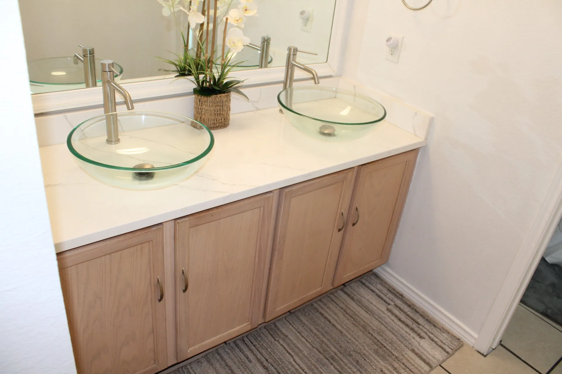 Double vanity featuring light wood-finish cabinetry, white countertop, and two glass vessel sinks with brushed nickel faucets