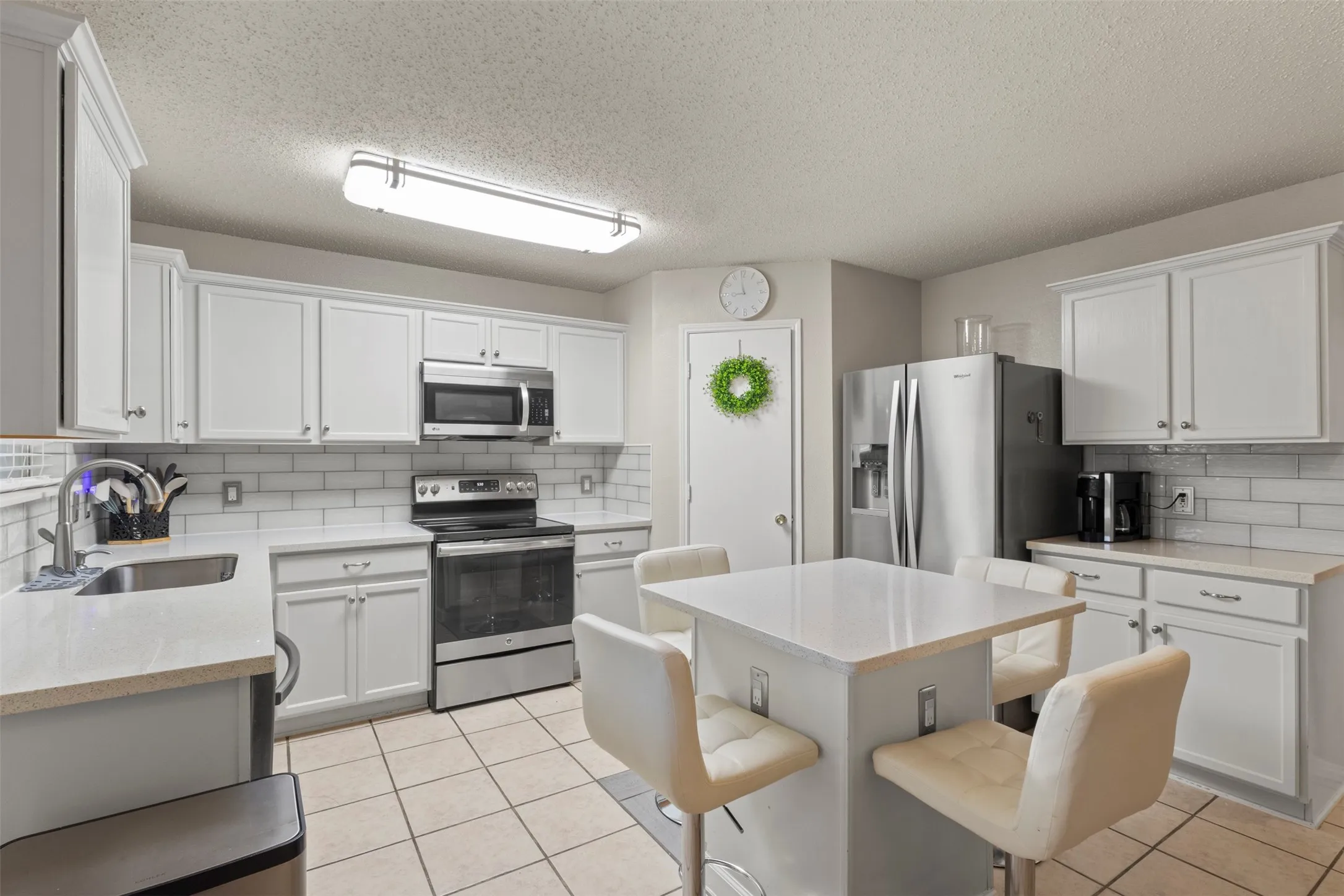 White shaker cabinetry with stainless steel appliances, subway tile backsplash, and a central island with integrated seating