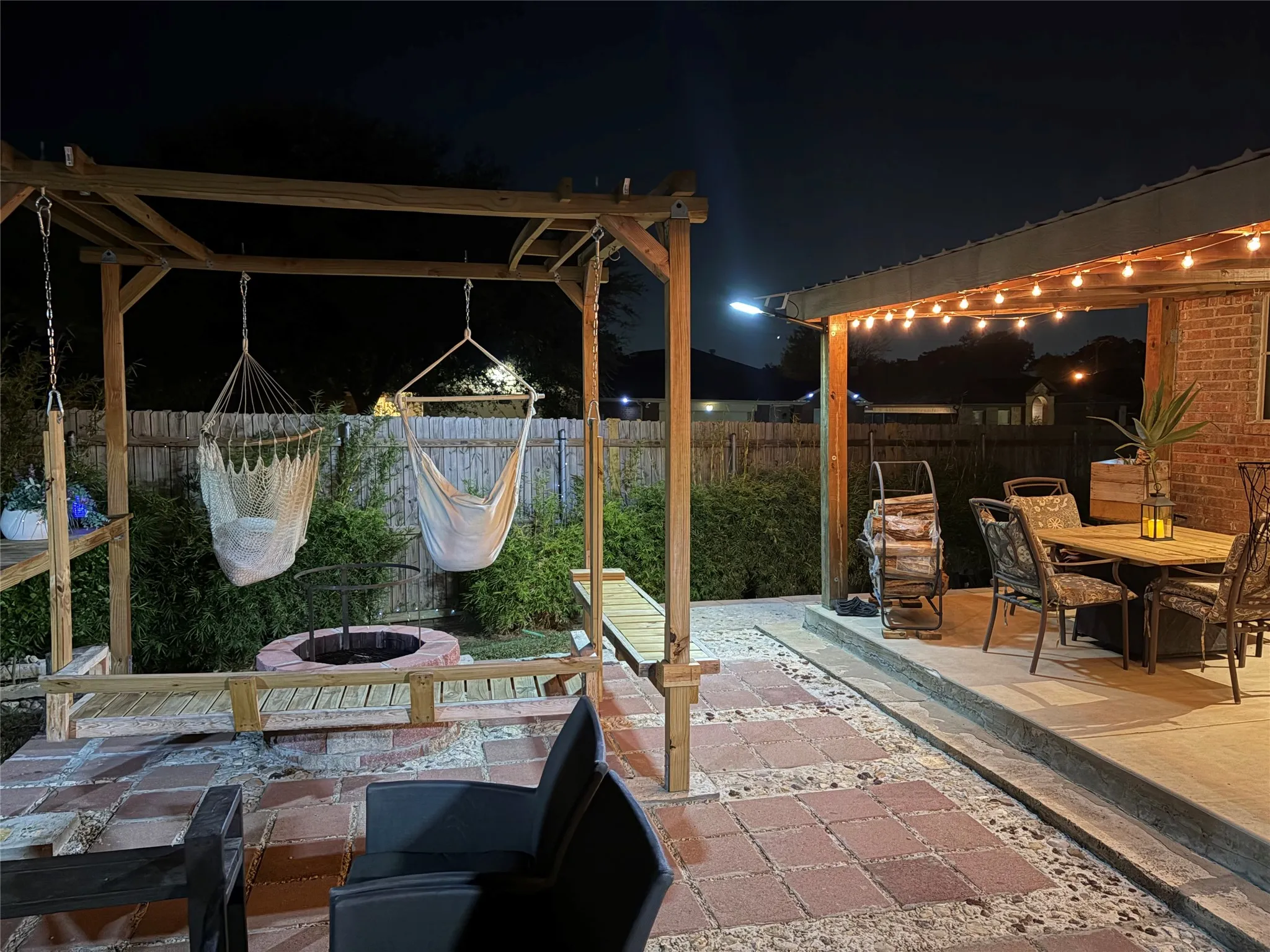 Expansive outdoor living area featuring a covered patio with string lighting, a wooden pergola, a built-in fire pit, and a paver stone walkway