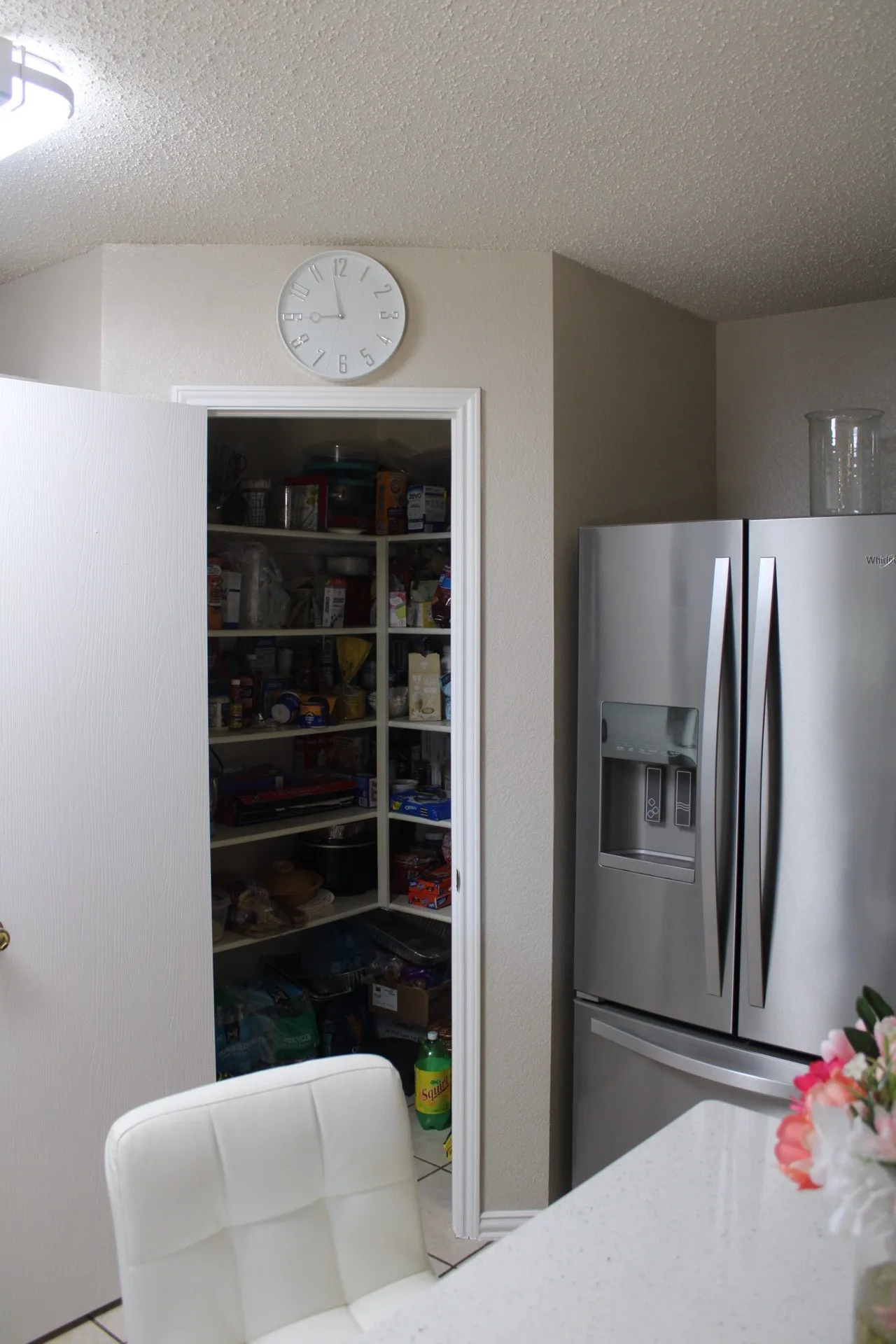 Walk-in corner pantry with shelving, stainless steel refrigerator, and light-toned countertop