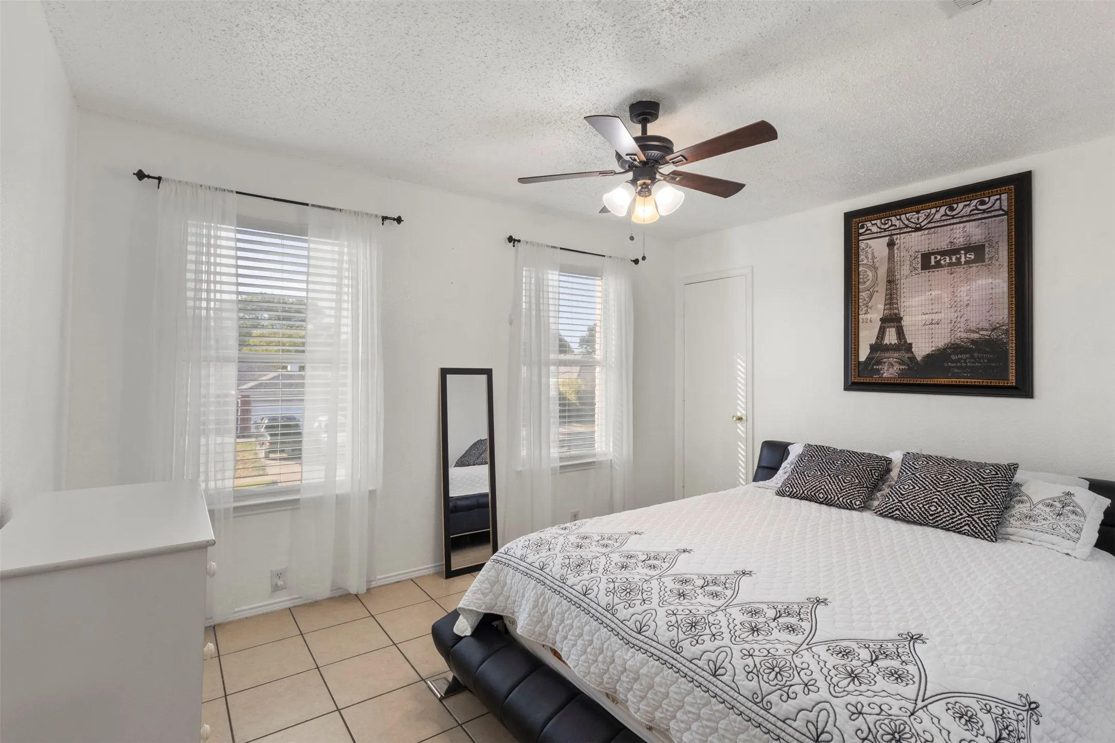 Tiled flooring, two windows with blinds, a ceiling fan with light fixture, and a solid door