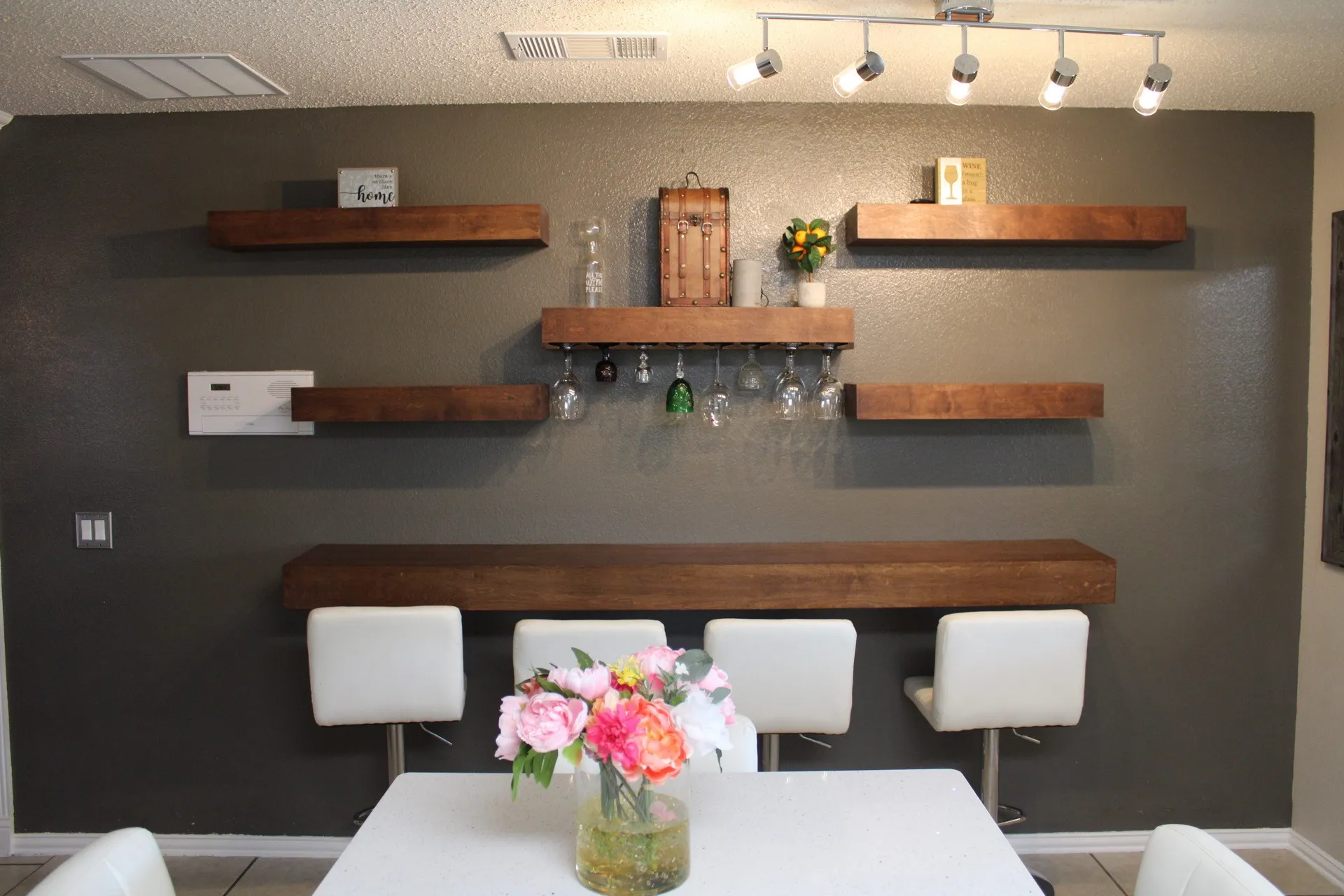 Accent wall with multiple wood-finish floating shelves, track lighting, and a built-in wood-finish bar