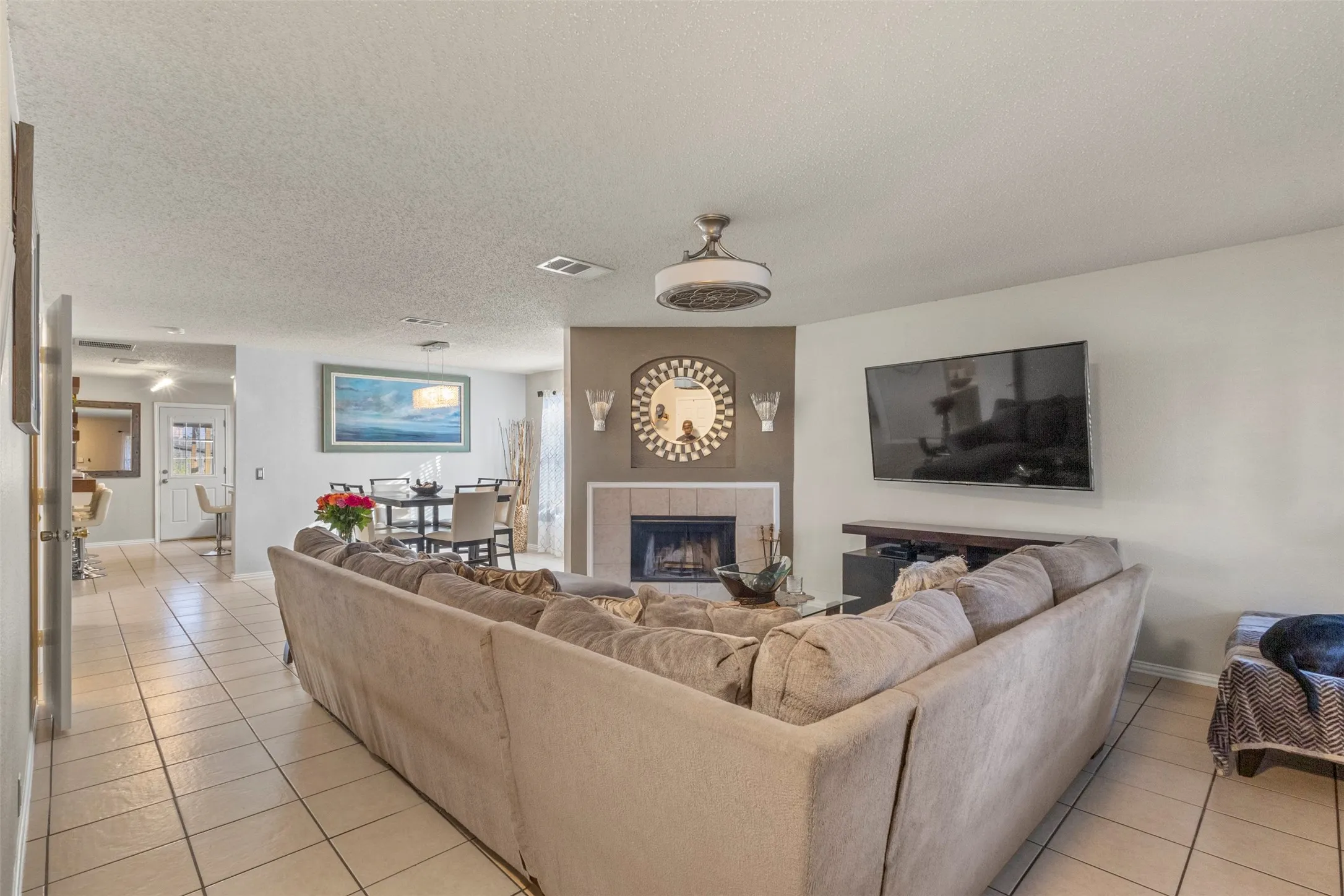 Living room featuring tile flooring, a fireplace with a mantel, and a ceiling fan
