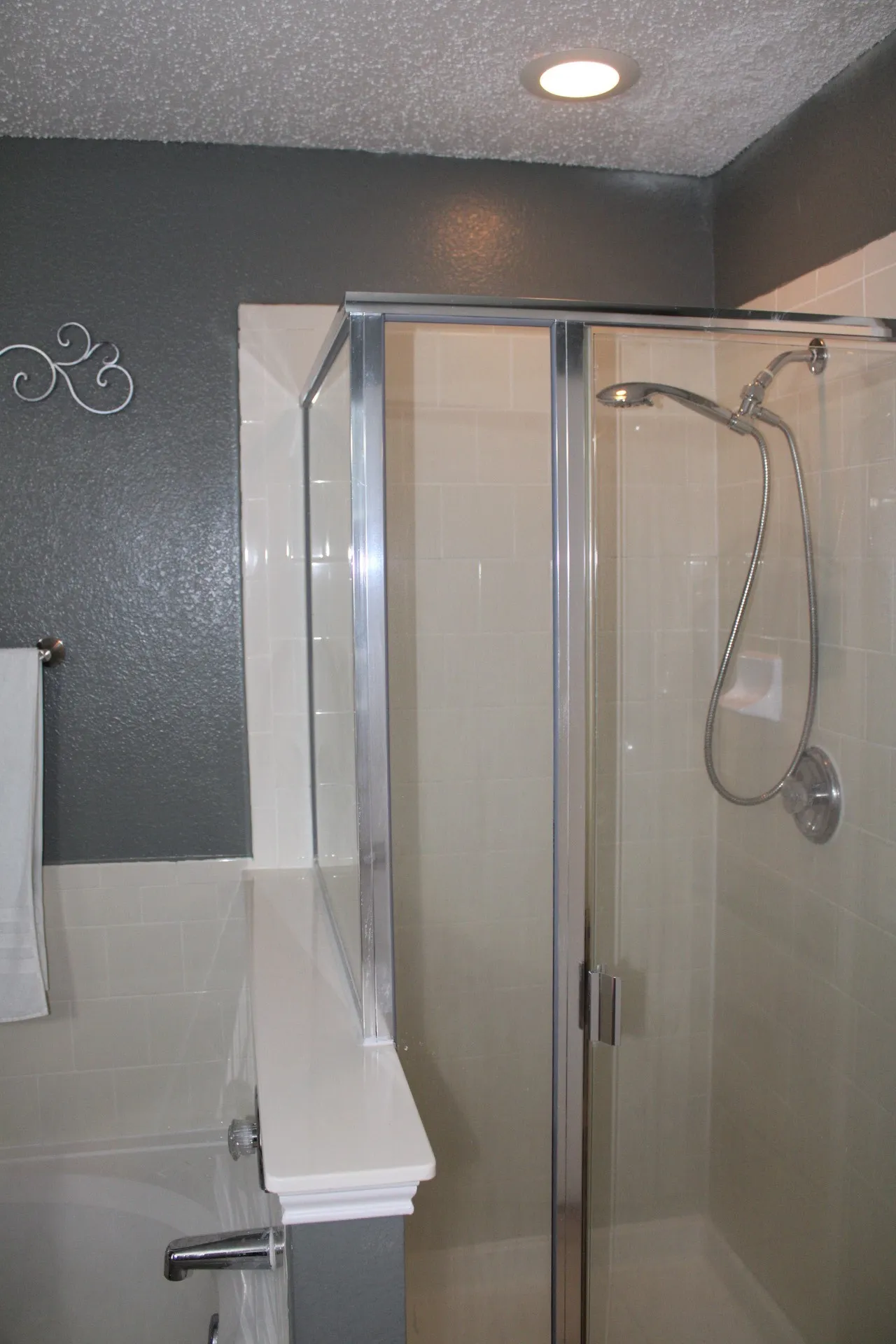 Shower with clear glass enclosure, tiled walls, and a built-in showerhead with a handheld sprayer