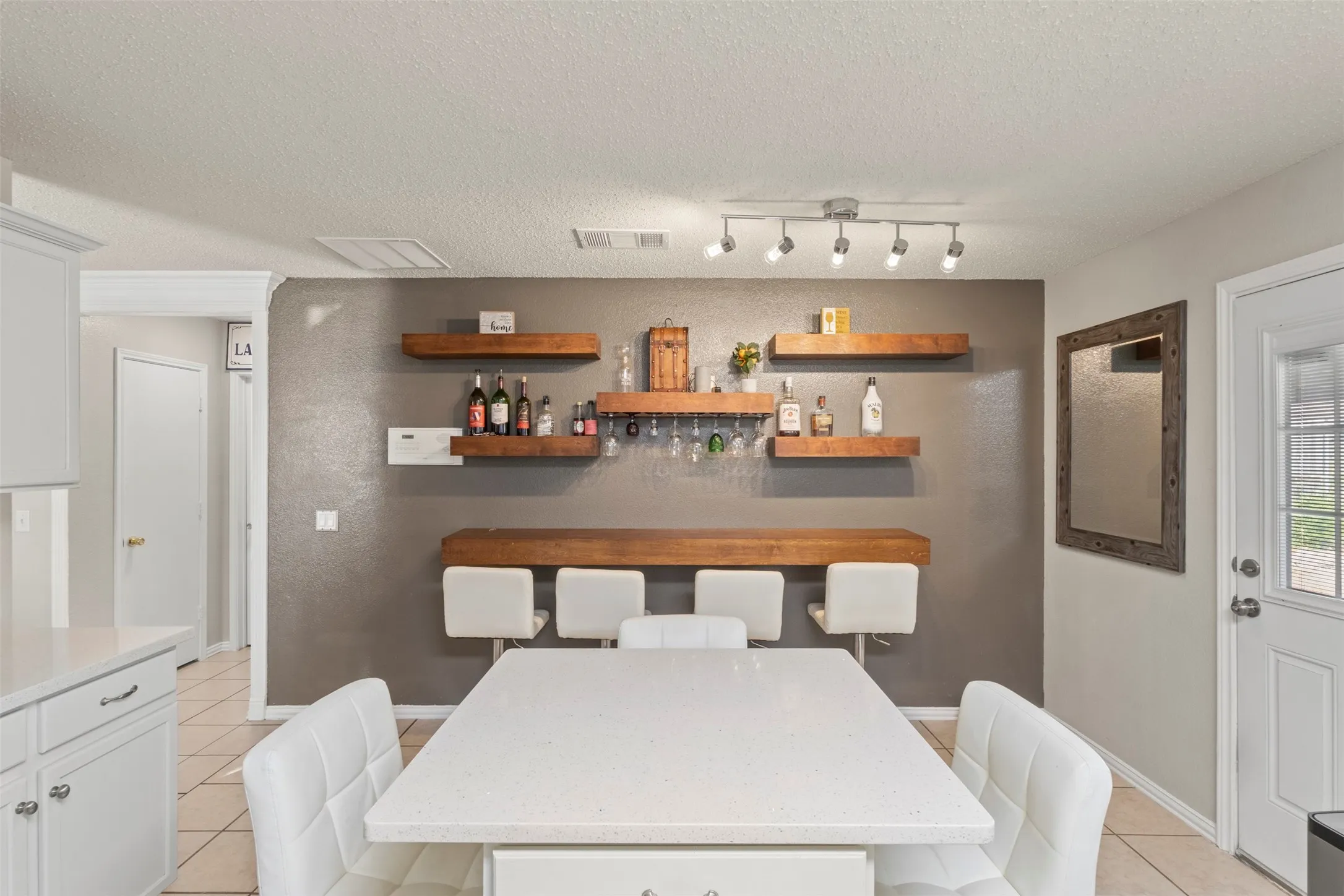 Built-in wood-finish shelving, wood-finish accent bar, track lighting, white kitchen cabinetry, and tile flooring