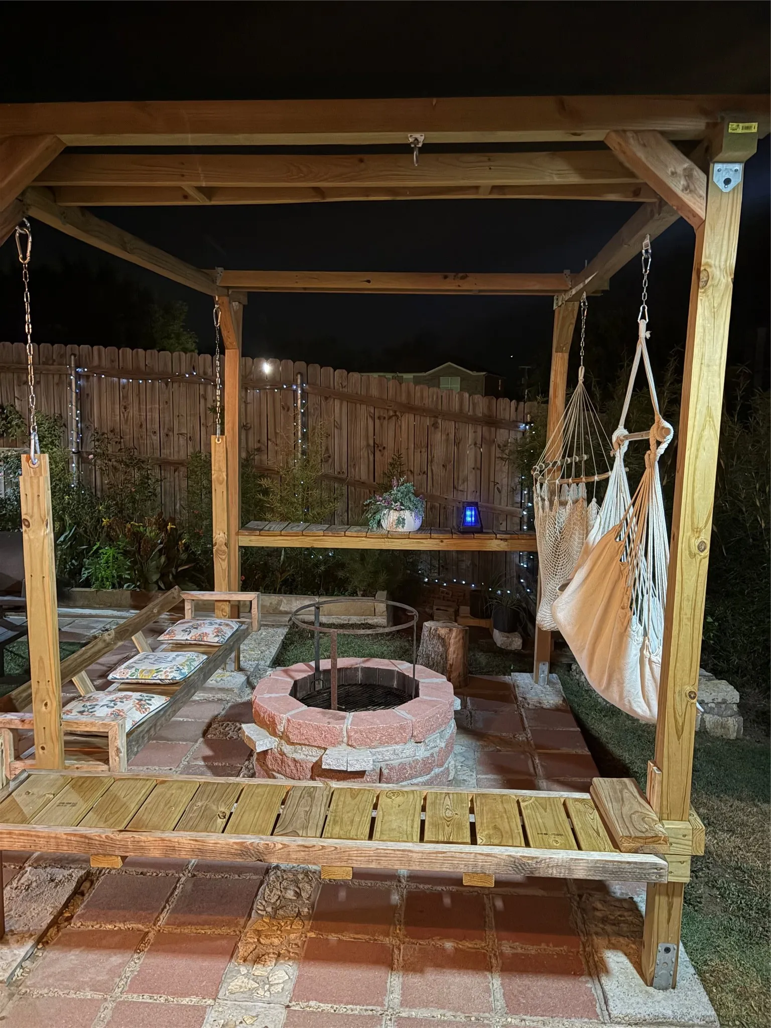 Wood pergola with integrated swing seating, brick patio, and a stone-lined fire pit