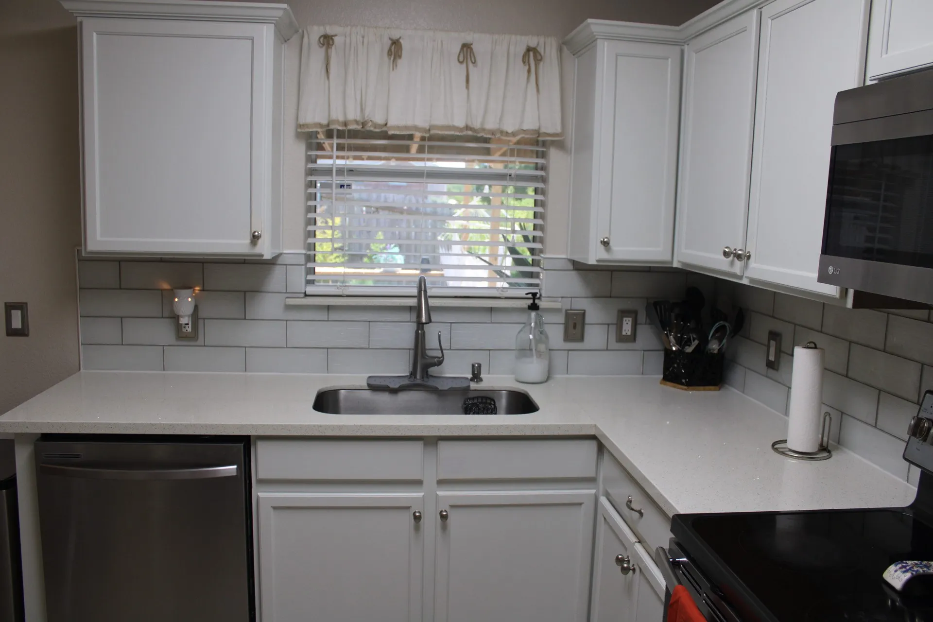 White shaker cabinetry, light-toned countertops, subway tile backsplash, stainless steel sink, and a built-in stainless steel dishwasher
