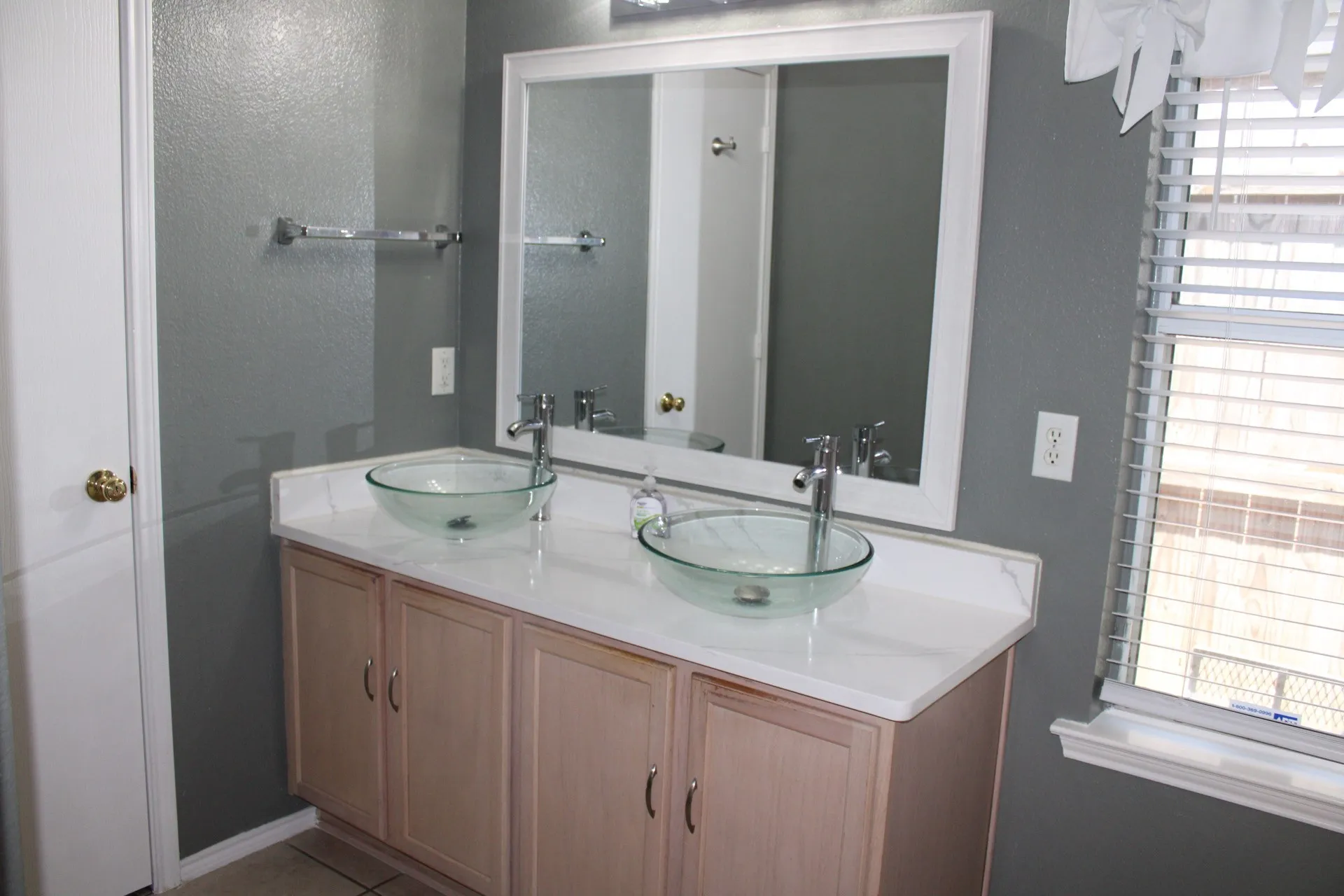 Dual vessel sinks with chrome fixtures, a light wood-finish vanity, and a framed mirror