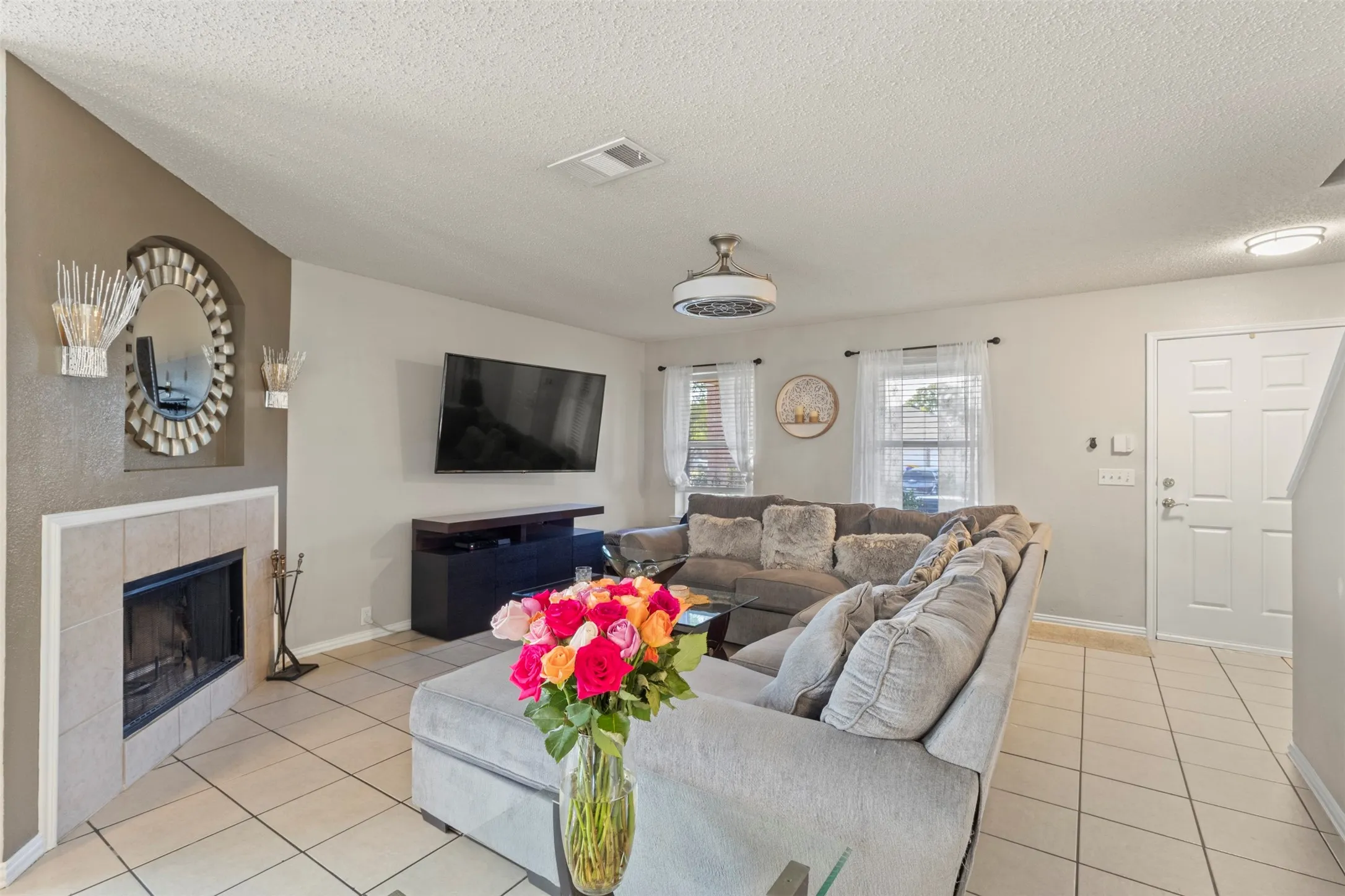 Living area featuring tile flooring, a fireplace with a light-colored tile surround, multiple windows with white blinds, and a built-in ceiling light fixture