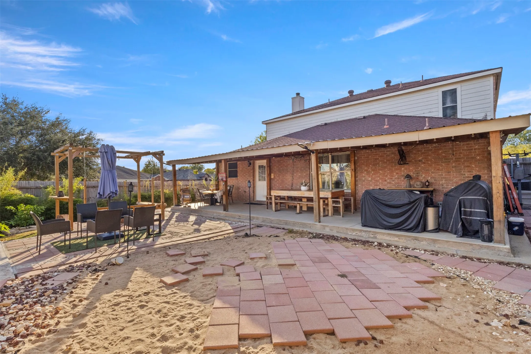 Expansive backyard featuring a covered patio, brick exterior, wood pergola, and partial paver patio