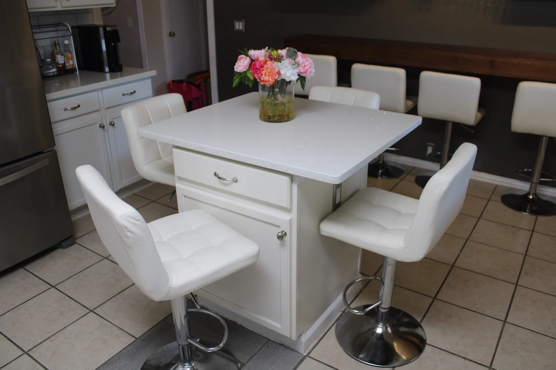Kitchen island with white countertop, white cabinetry with silver hardware, and tile flooring