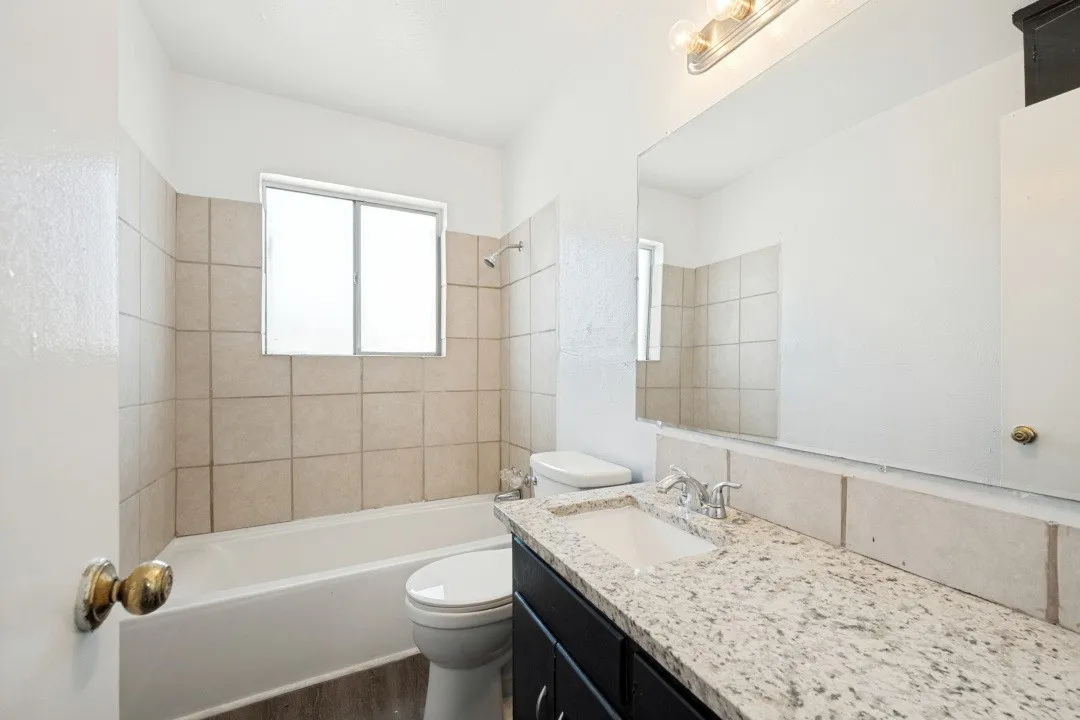 Bathroom featuring a tub/shower combination with tiled surround, a vanity with a light-colored countertop, and a large wall-mounted mirror