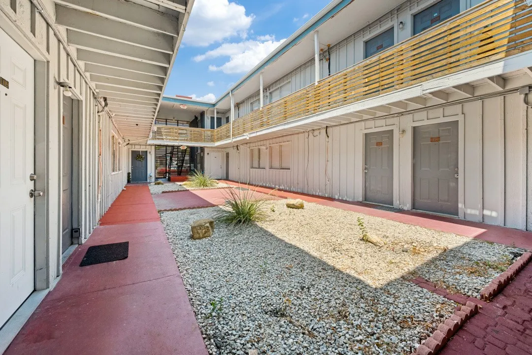 Multi-level courtyard building featuring wood-paneled siding, upper-level balconies with wood slatted railings, and a central gravel landscape with integrated plantings