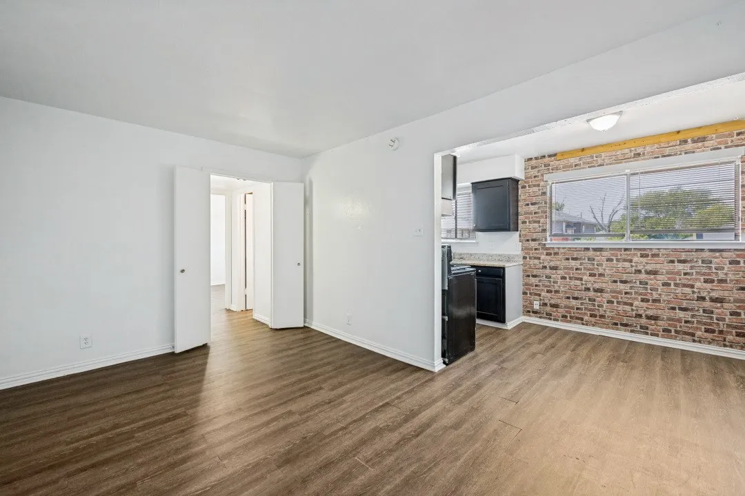 Wood-finish flooring throughout, white interior walls, exposed brick accent wall, black cabinetry, and a built-in window