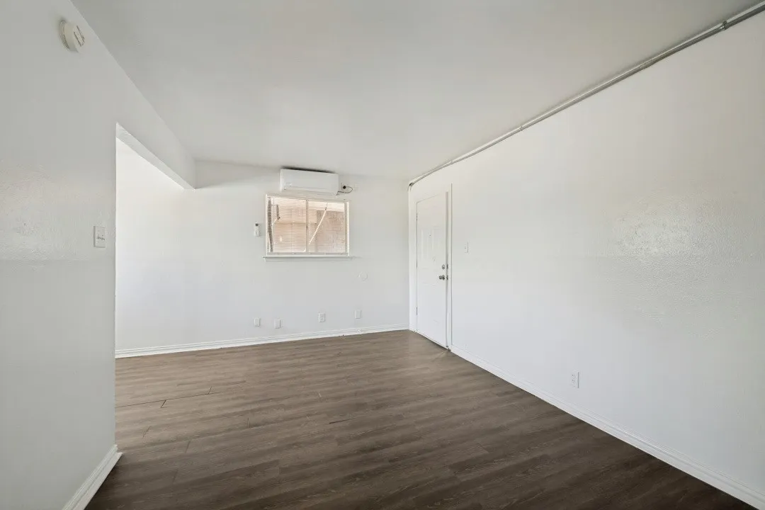 Wood-finish flooring with white walls and a window air conditioning unit