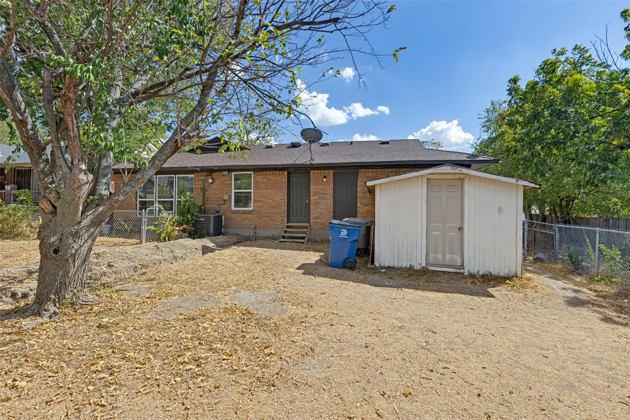 Brick exterior residence with a composition shingle roof, rear entry door with wooden steps, and an exterior storage shed