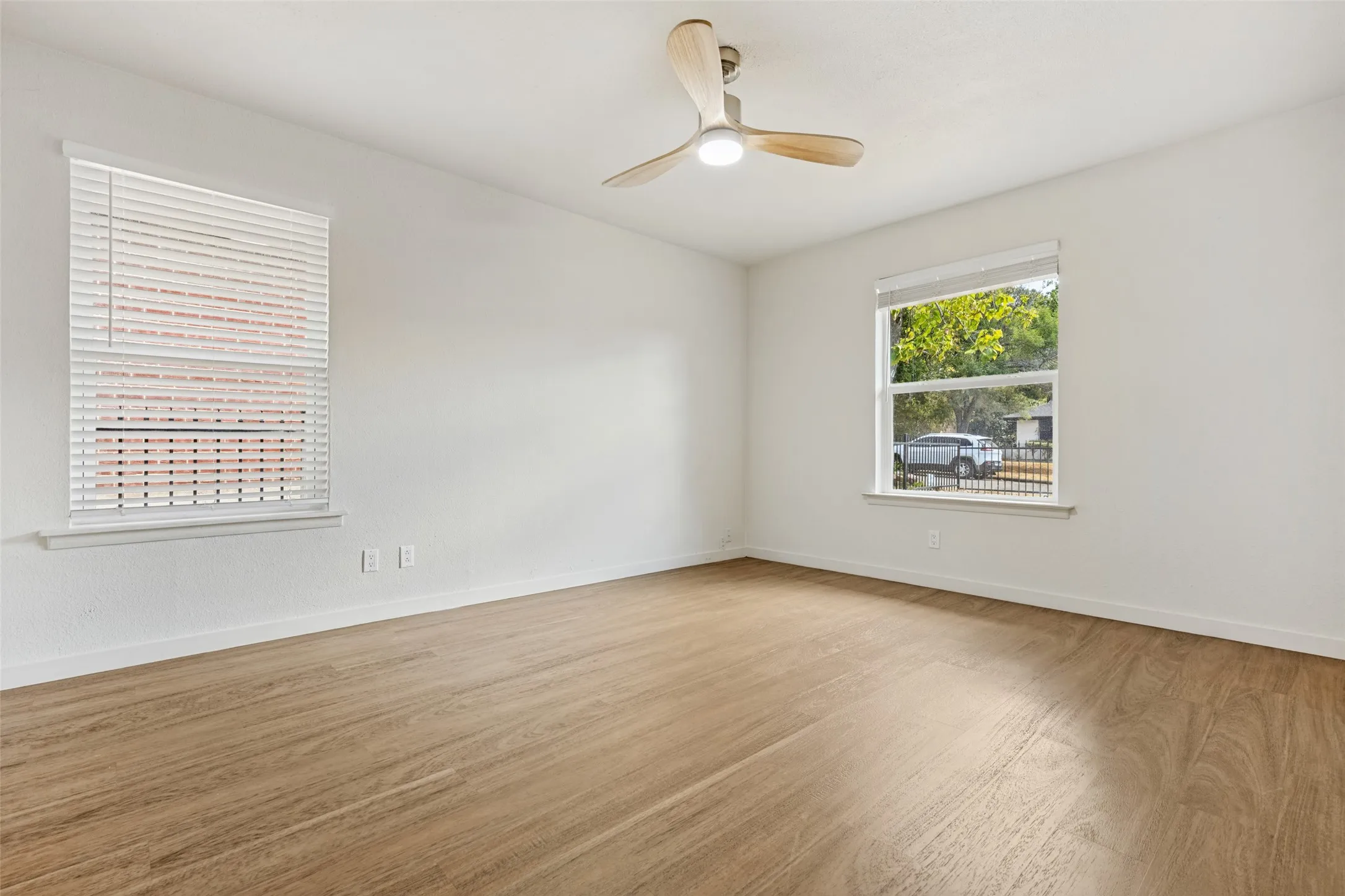 Wood-finish flooring, white walls, two windows with blinds, and a ceiling fan with integrated lighting