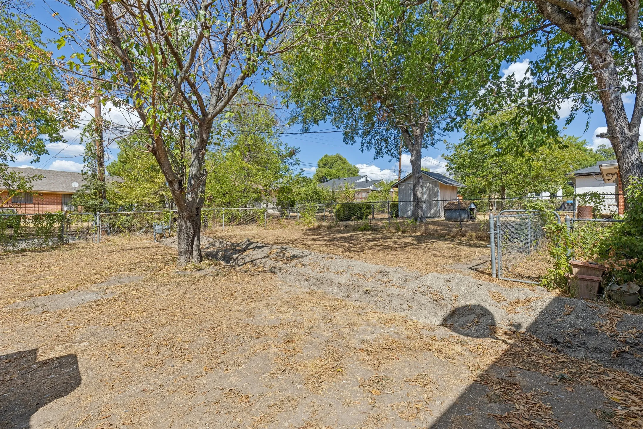 Expansive rear yard featuring mature trees, chain-link fencing, and a detached storage shed