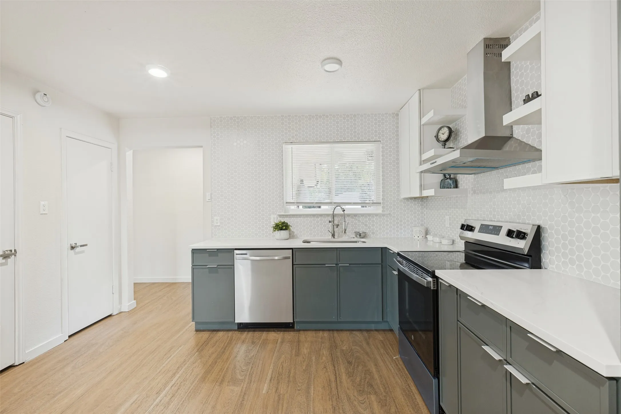 Contemporary kitchen featuring wood-finish flooring, white solid surface countertops, and a hexagonal tile backsplash