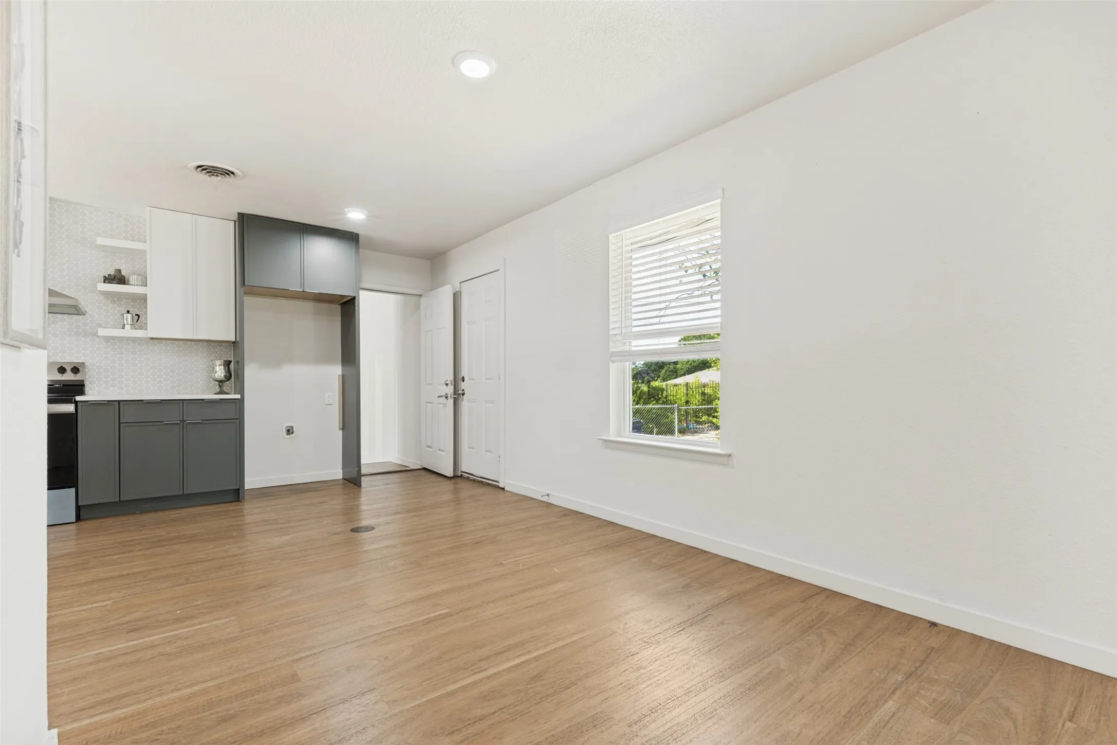 Wood-finish flooring throughout, bright white walls, modern kitchen with two-tone cabinetry, geometric tile backsplash, and recessed lighting
