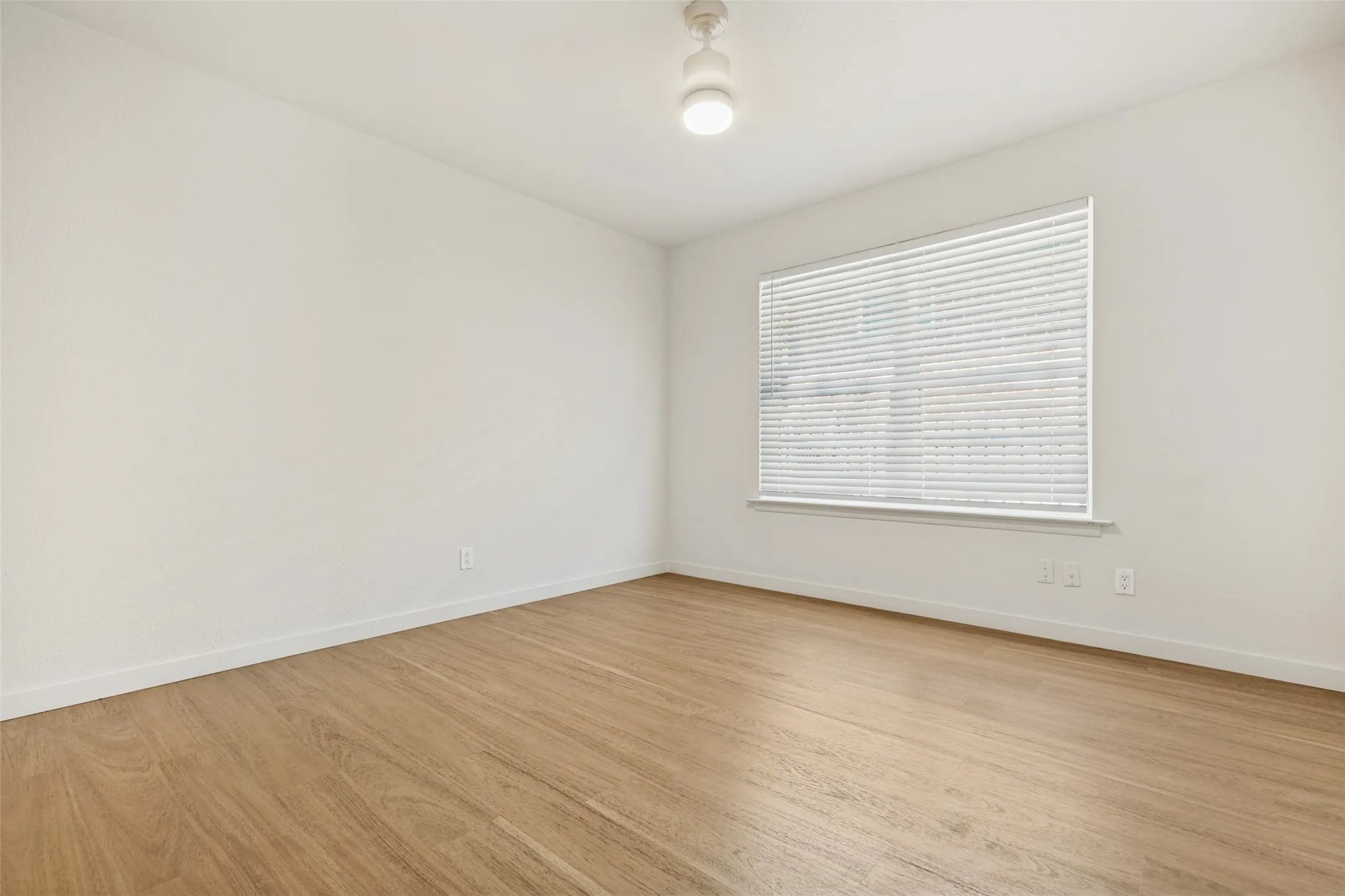 Wood-finish flooring with crisp white walls, a large window, and a ceiling-mounted light fixture