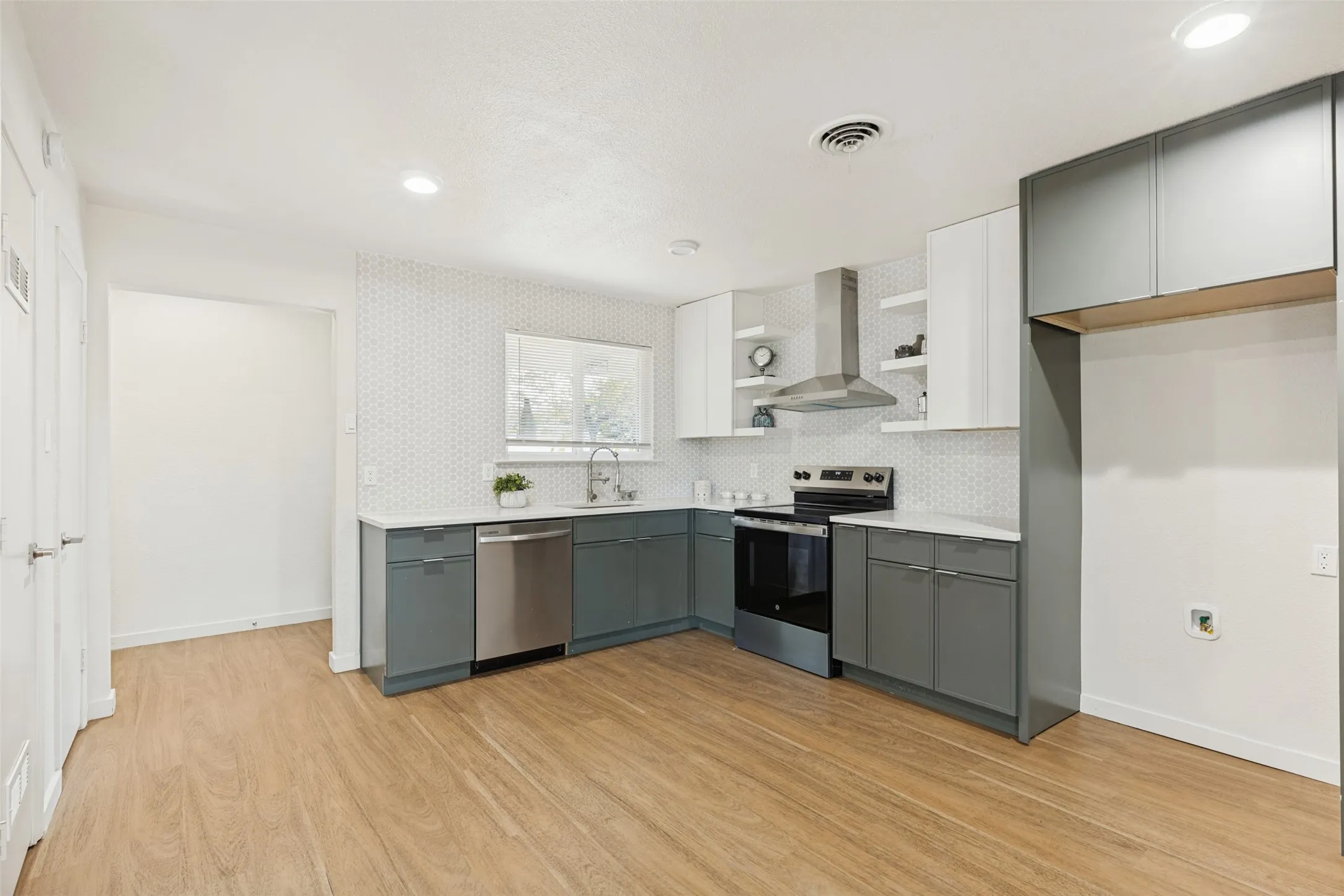 Kitchen featuring wood-finish flooring, two-tone cabinetry, stainless steel appliances, a tile backsplash, and recessed lighting