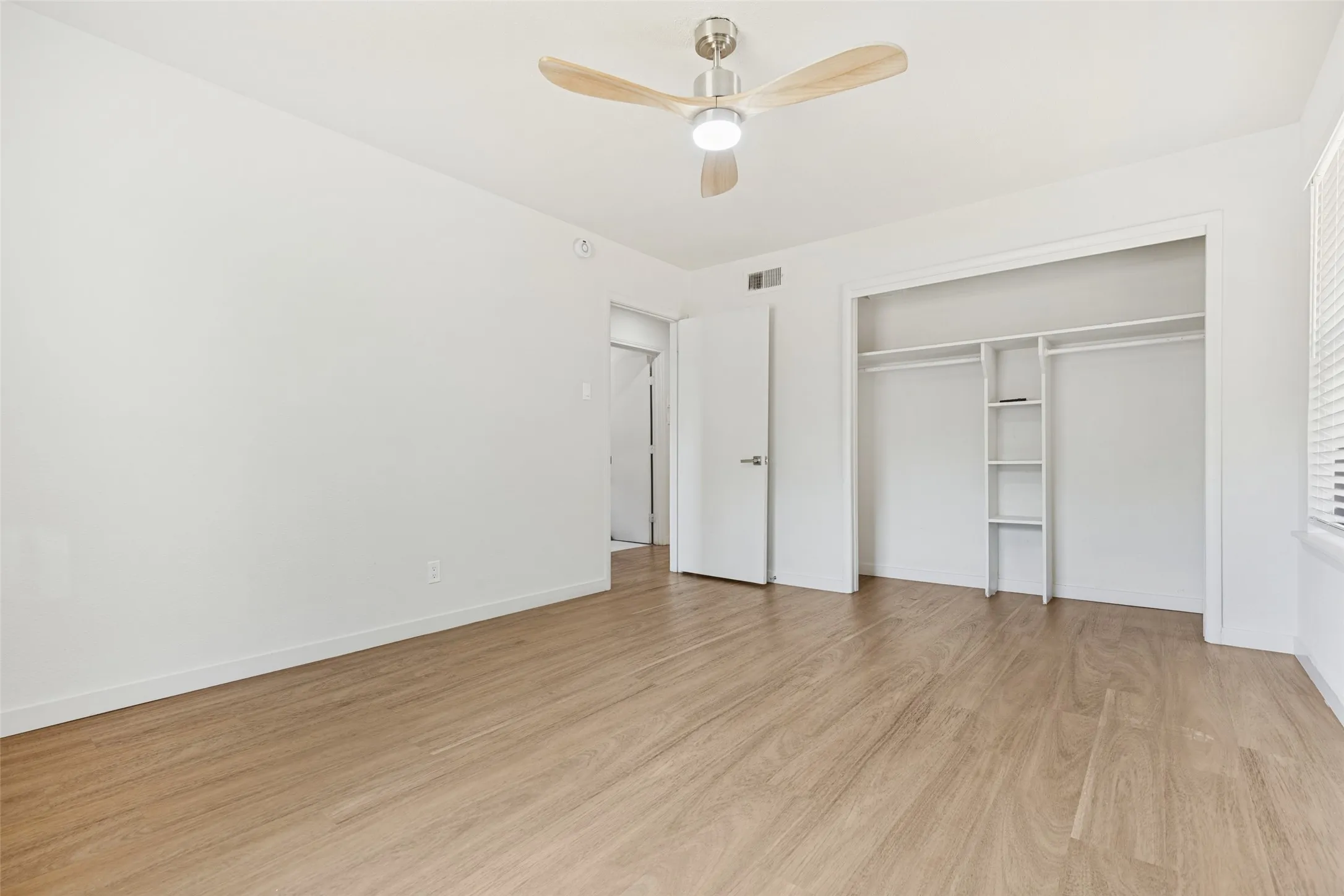 Wood-finish flooring, white walls, ceiling fan with integrated lighting, built-in closet shelving, and a window with horizontal blinds