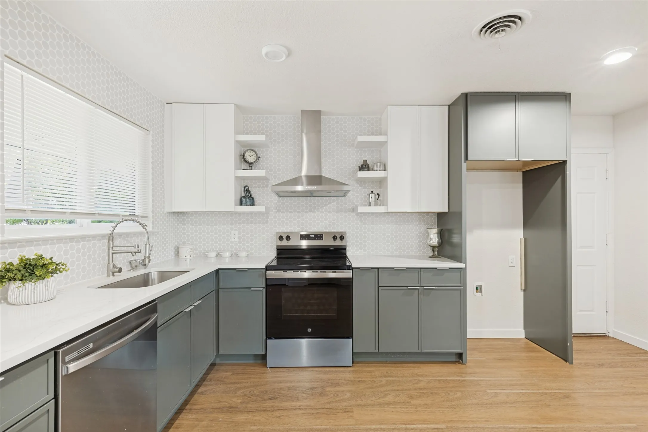 Kitchen featuring wood-finish flooring, two-tone cabinetry, stainless steel appliances, a tile backsplash, and white countertops