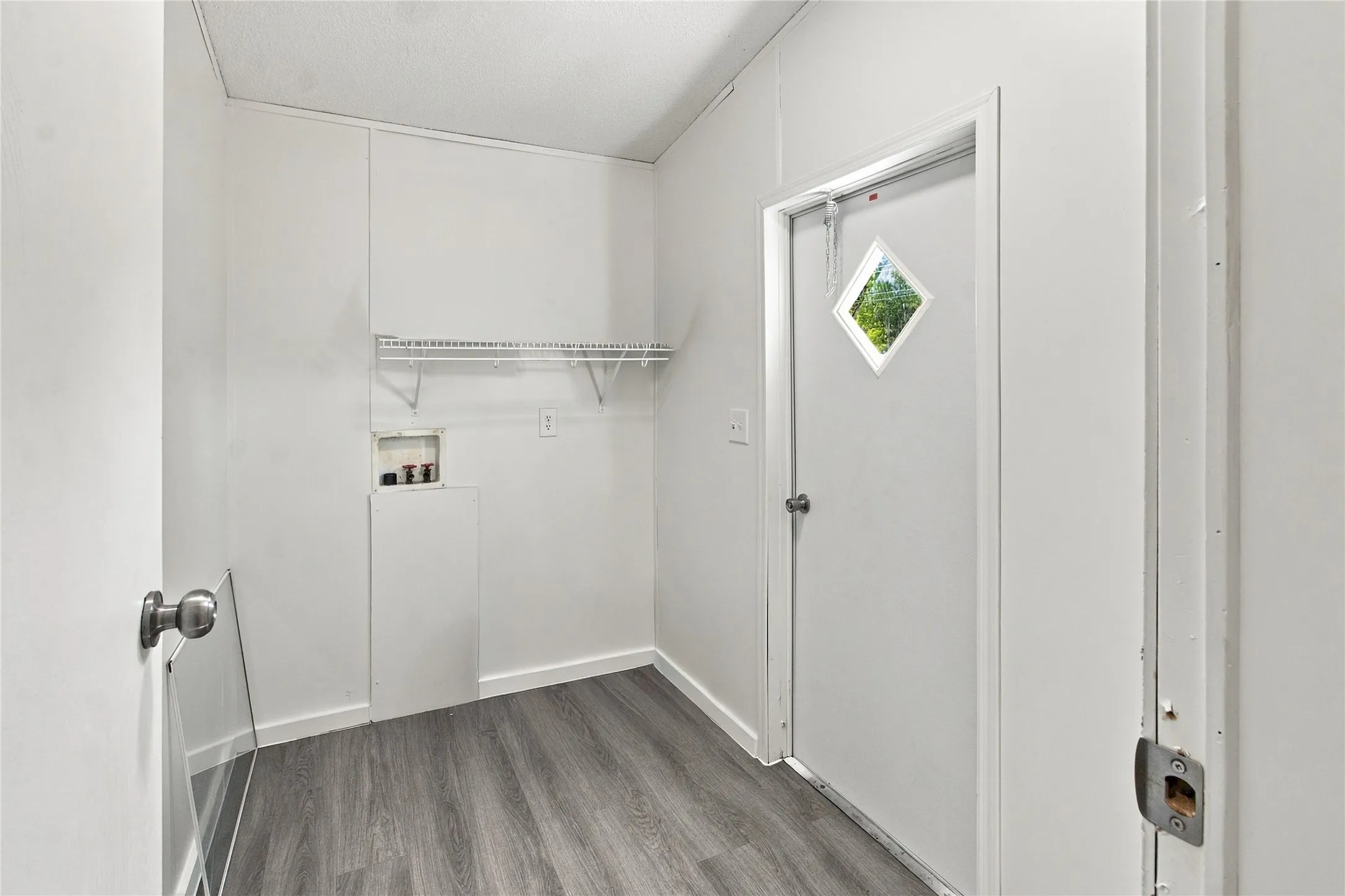 White walls and wood-finish flooring with a diamond-paneled door