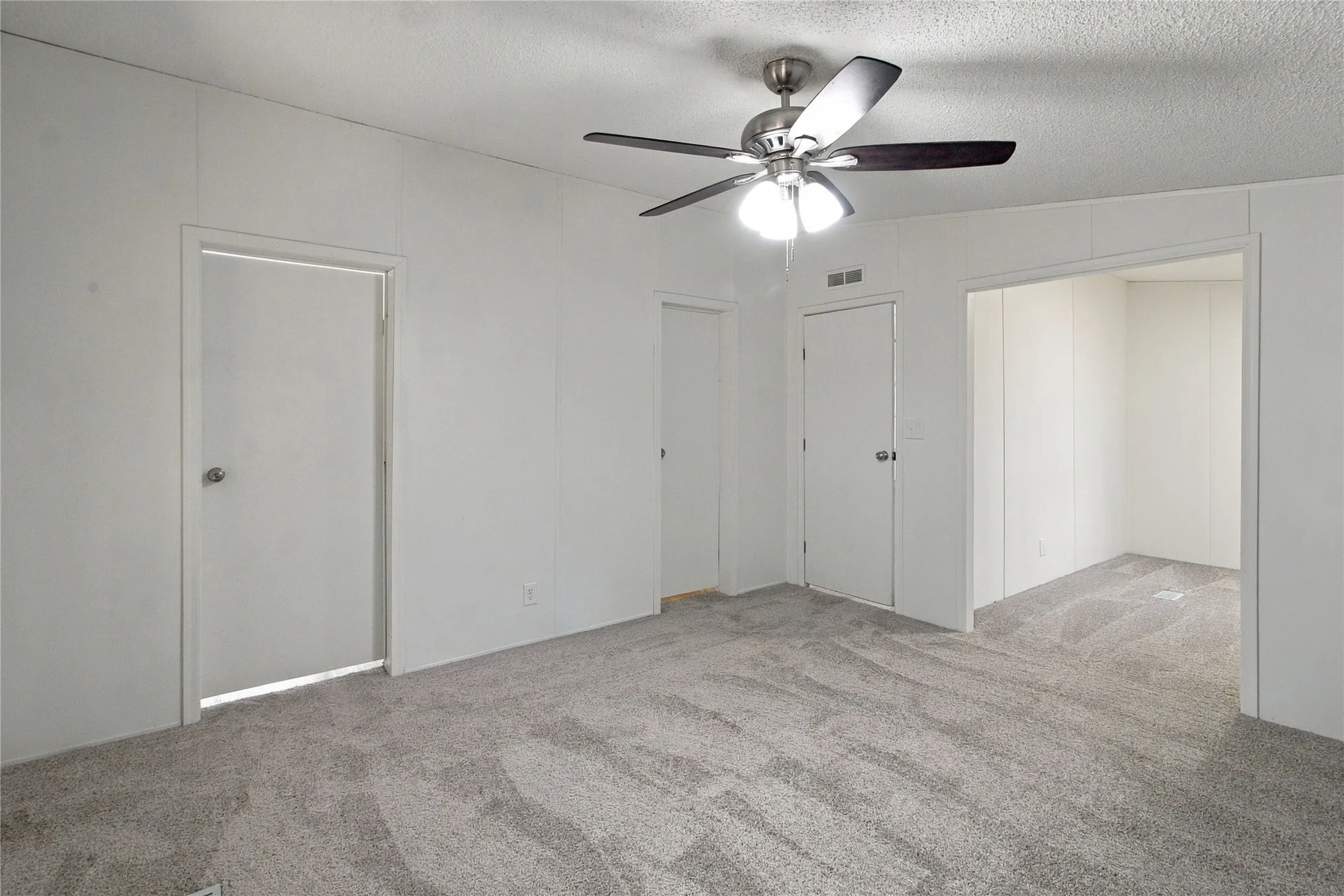 Gray carpeting throughout, white paneled walls, and a ceiling fan with integrated lighting