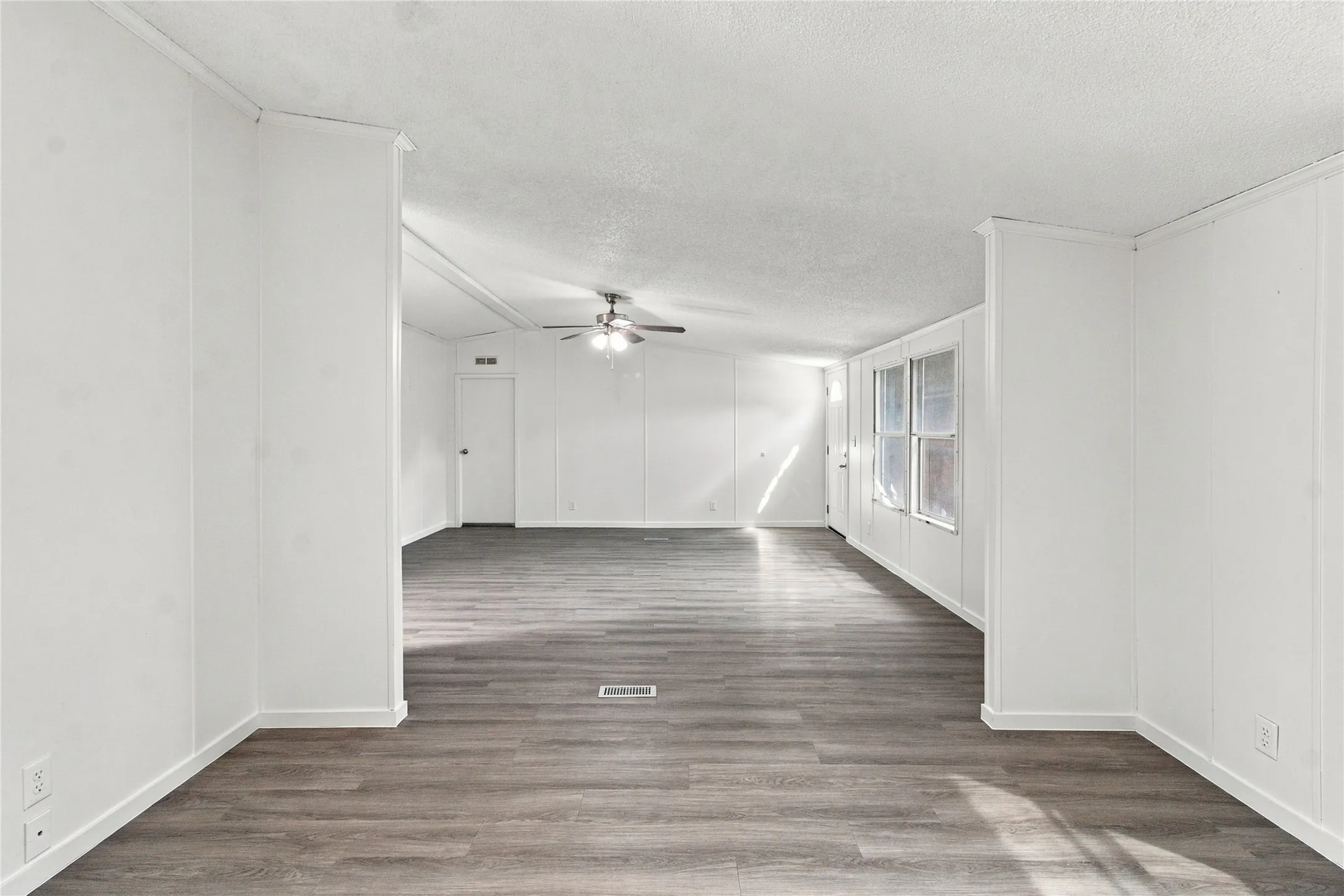 Spacious interior featuring wood-finish flooring, white paneled walls, multiple windows, and a ceiling fan