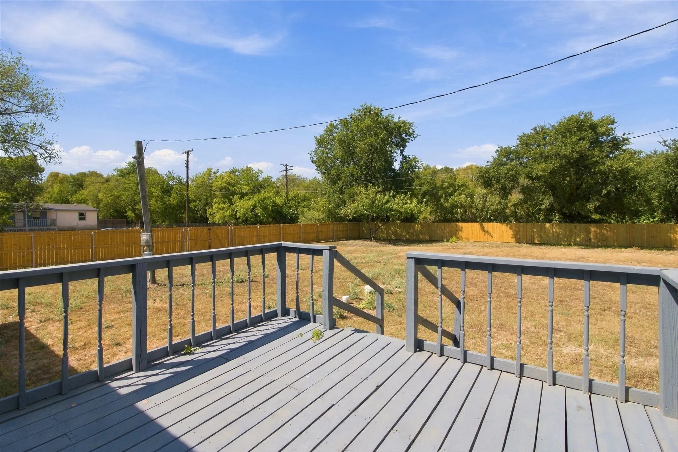 Expansive backyard featuring a wood deck with railings and a perimeter privacy fence