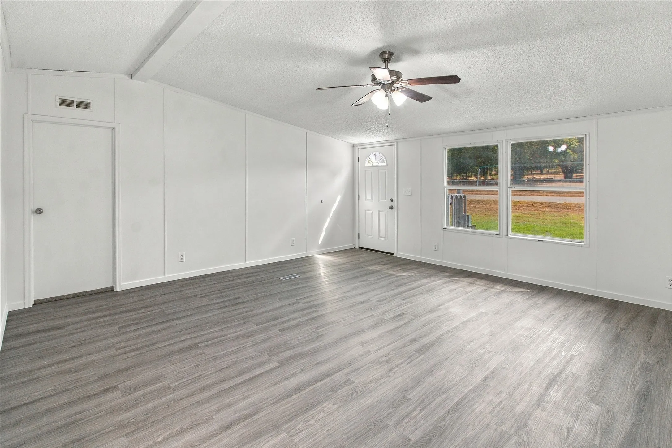 Spacious room featuring wood-finish flooring, white cabinetry along one wall, a ceiling fan with integrated lighting, and glass sliding doors opening to outdoor space
