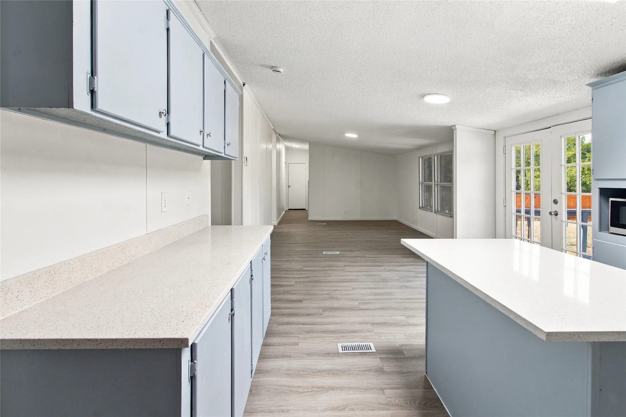 Light-toned countertops with blue cabinetry, wood-finish flooring, recessed lighting, and double glass-paneled doors