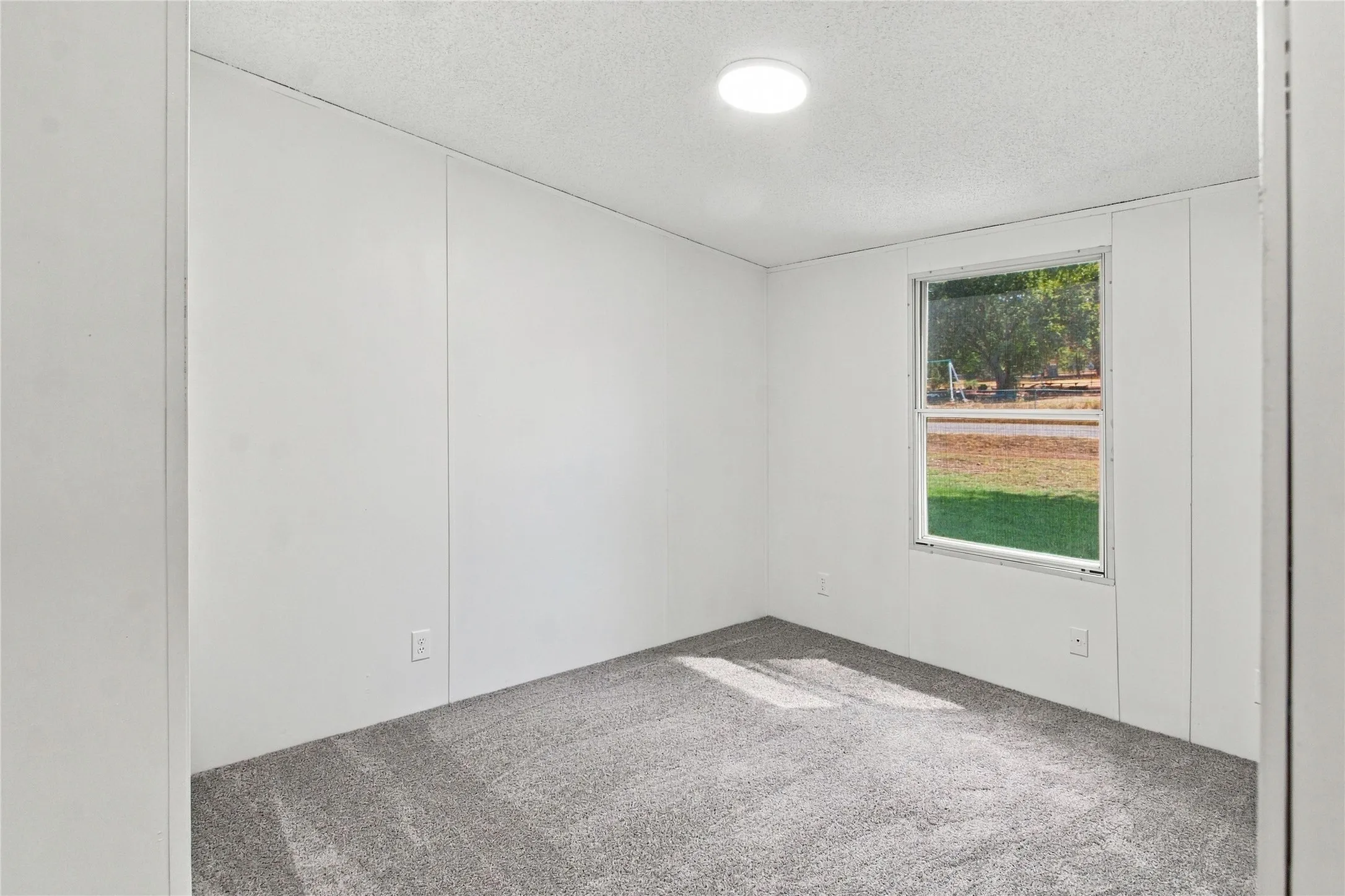 Recessed ceiling light, single window, gray carpeting, and white wall panels