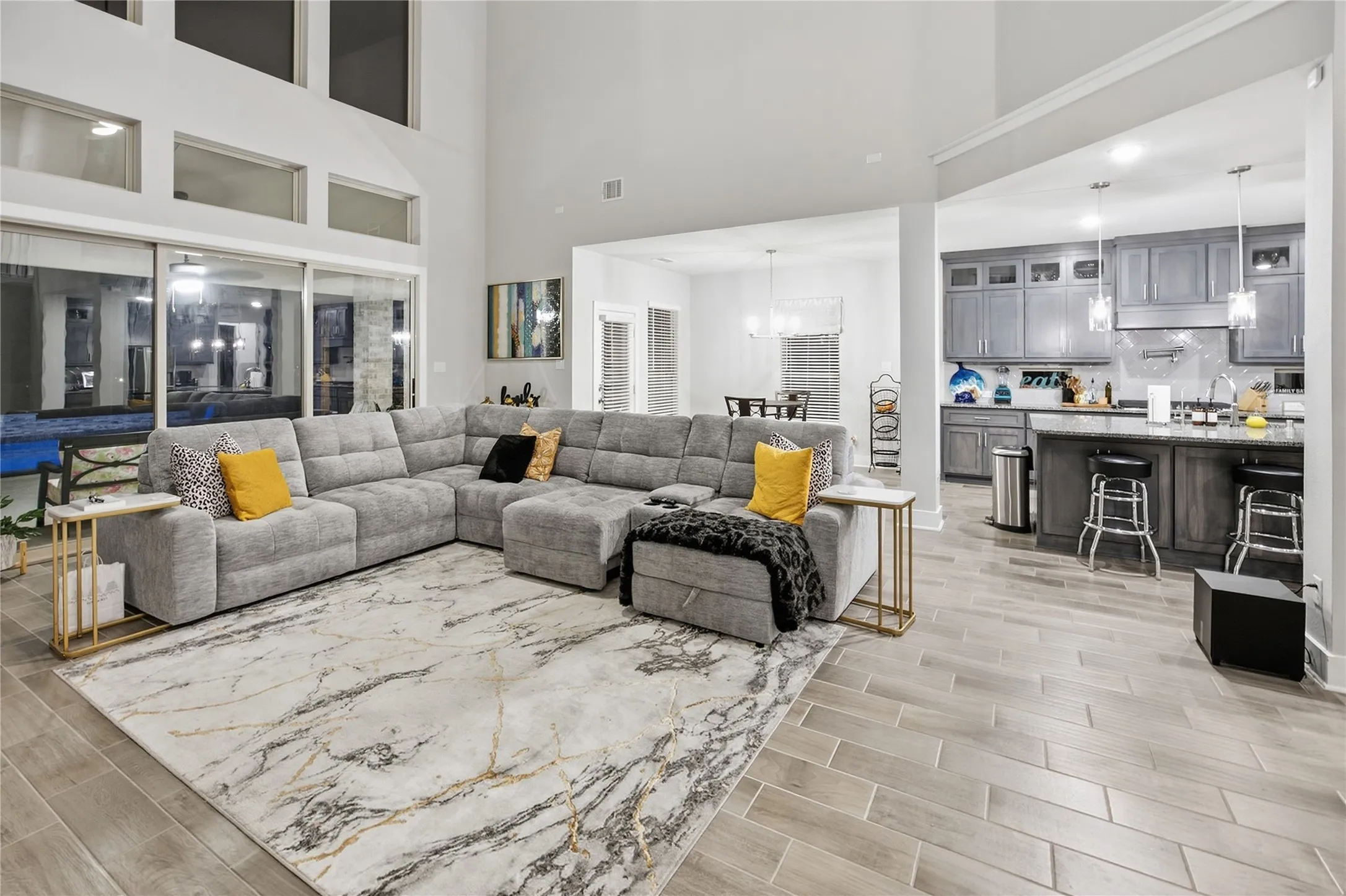Vaulted ceiling with transom windows, full-height sliding glass doors, tile flooring, kitchen with dark wood-finish cabinetry, and a kitchen island with seating